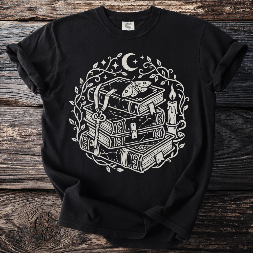 Black t-shirt with a circular graphic of stacked books, a key, moth, candle, and moon.