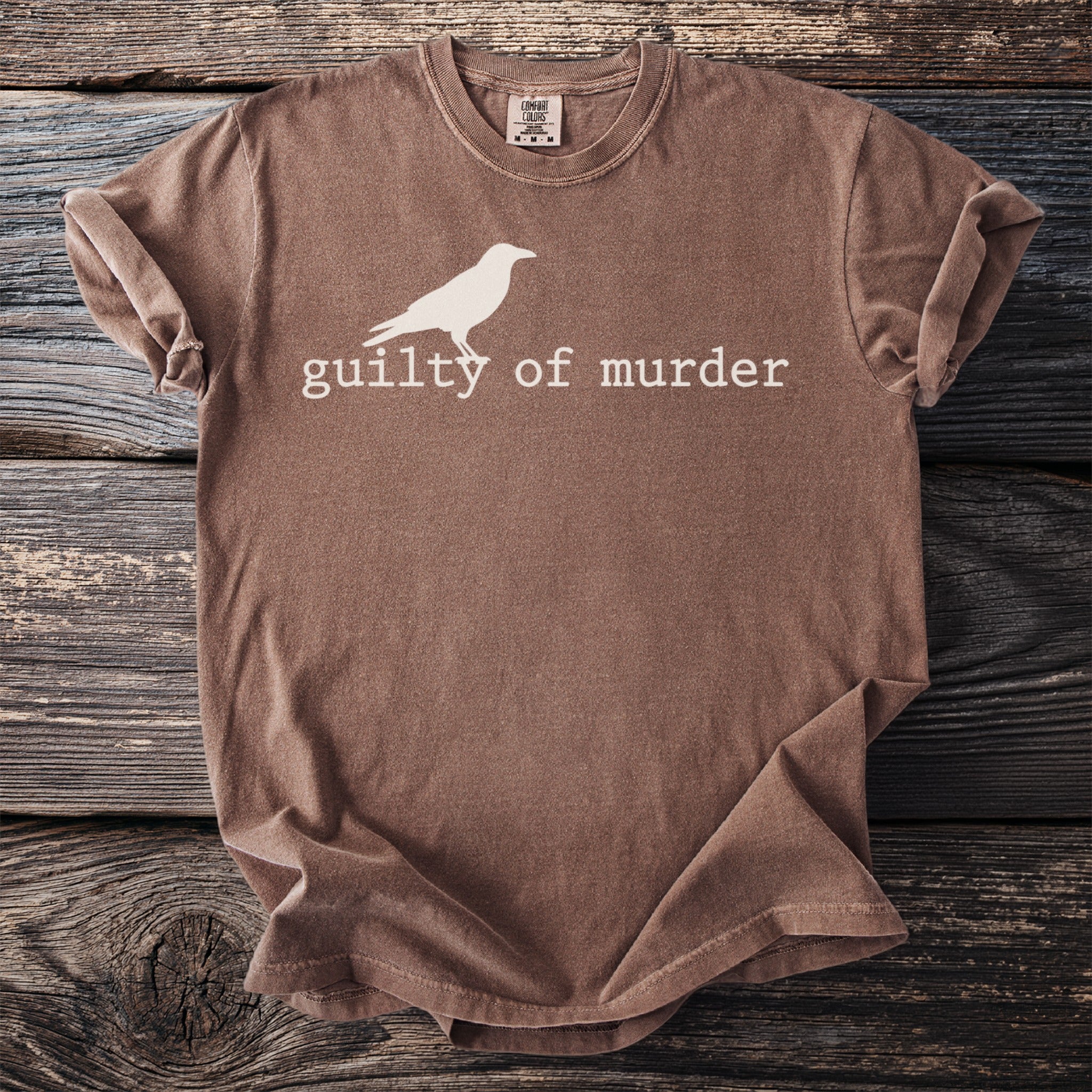 Brown t-shirt with a white bird graphic and "guilty of murder" text.
