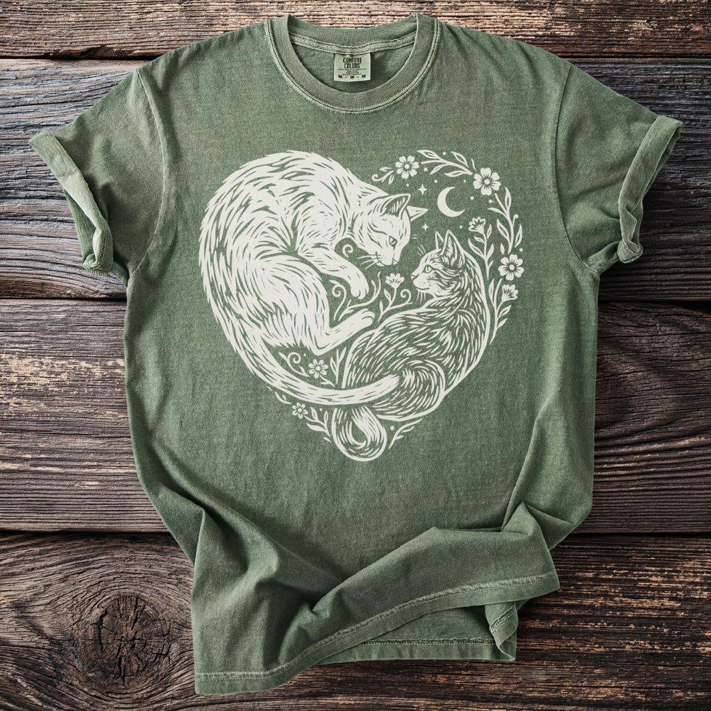 Green t-shirt with a white heart-shaped design of two cats surrounded by flowers and a moon.