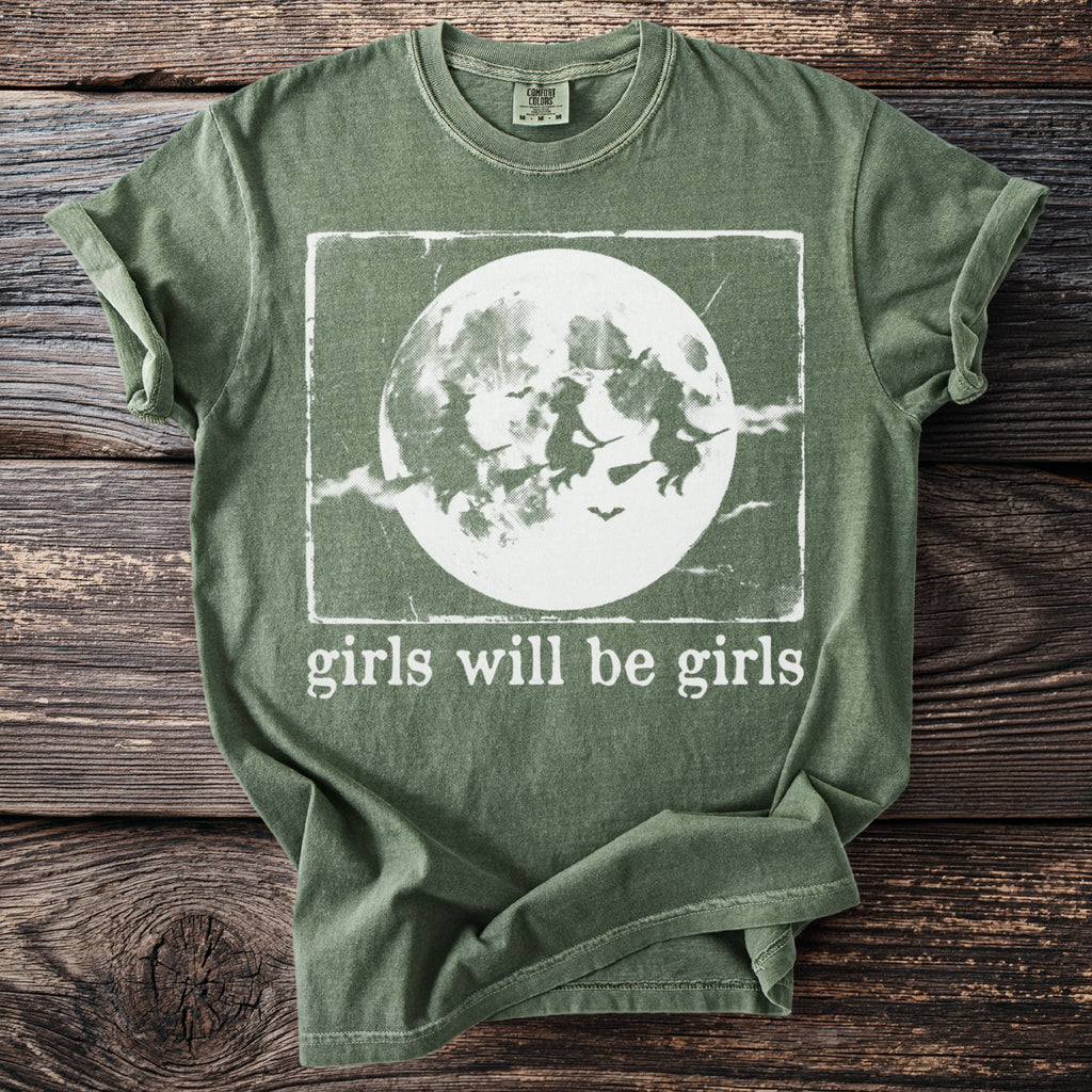 Green t-shirt with witches flying in front of a moon and "girls will be girls" text.