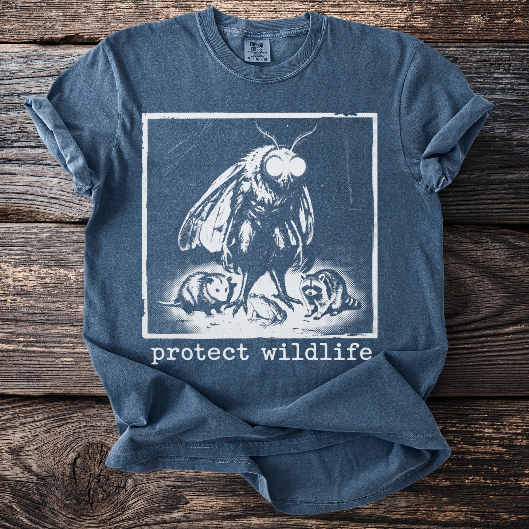 Blue t-shirt with a moth, opossum, frog, and raccoon graphic and "protect wildlife" text.