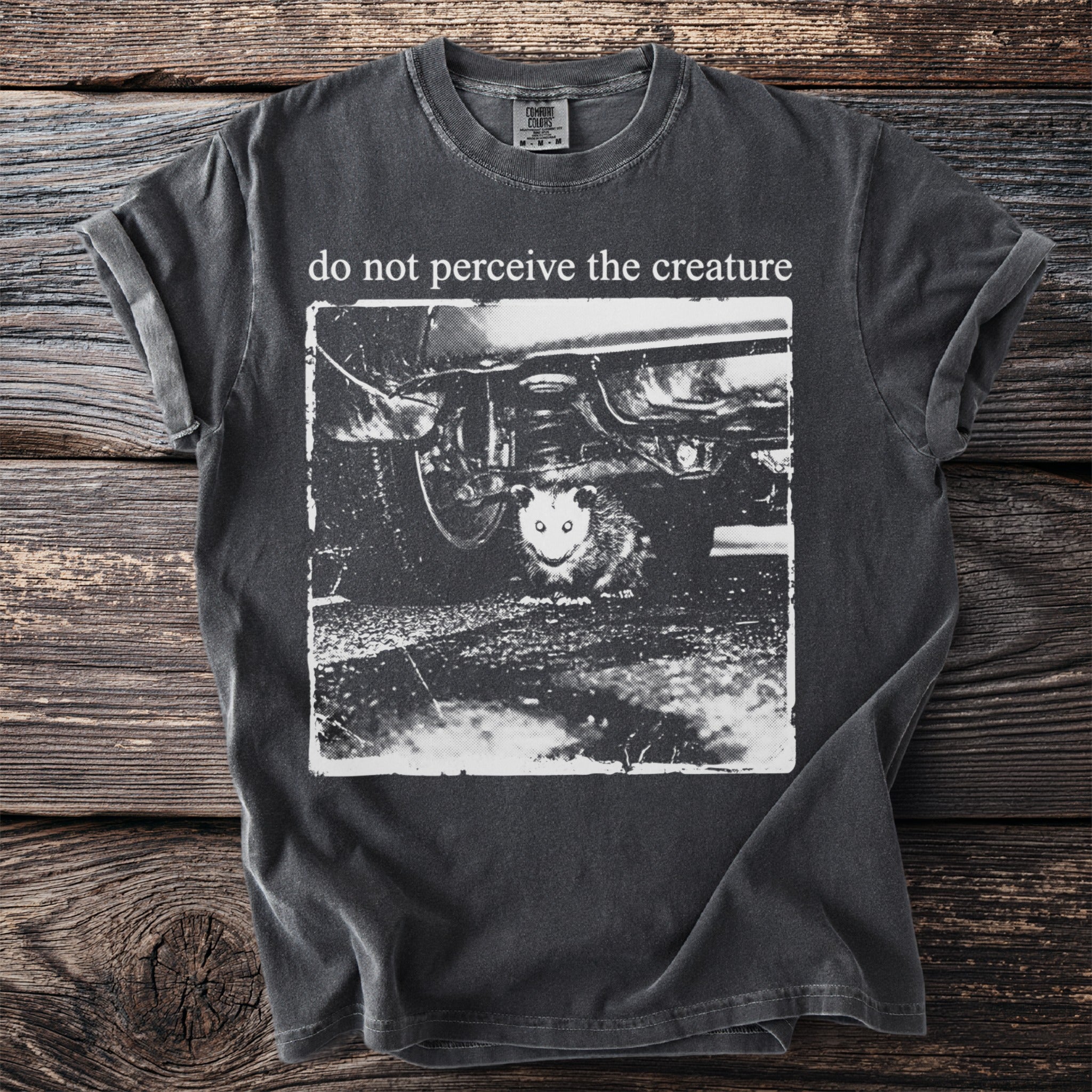 Dark t-shirt with "do not perceive the creature" and a possum under a car.