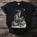 Black t-shirt with a cream folk-cut print: Krampus sits on a snowy log reading a small book by the light of one candle.