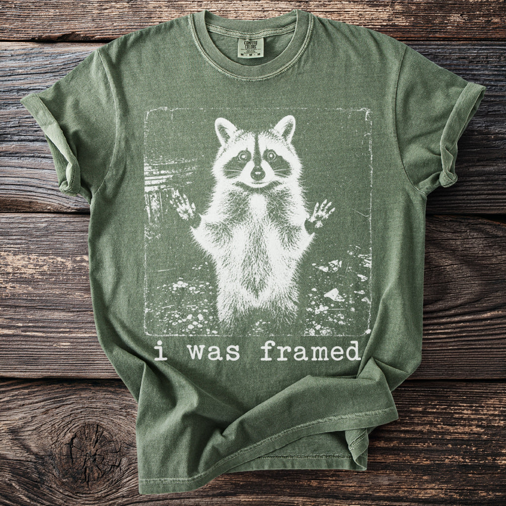 Green t-shirt with a distressed print of a raccoon with raised paws and the text "i was framed."