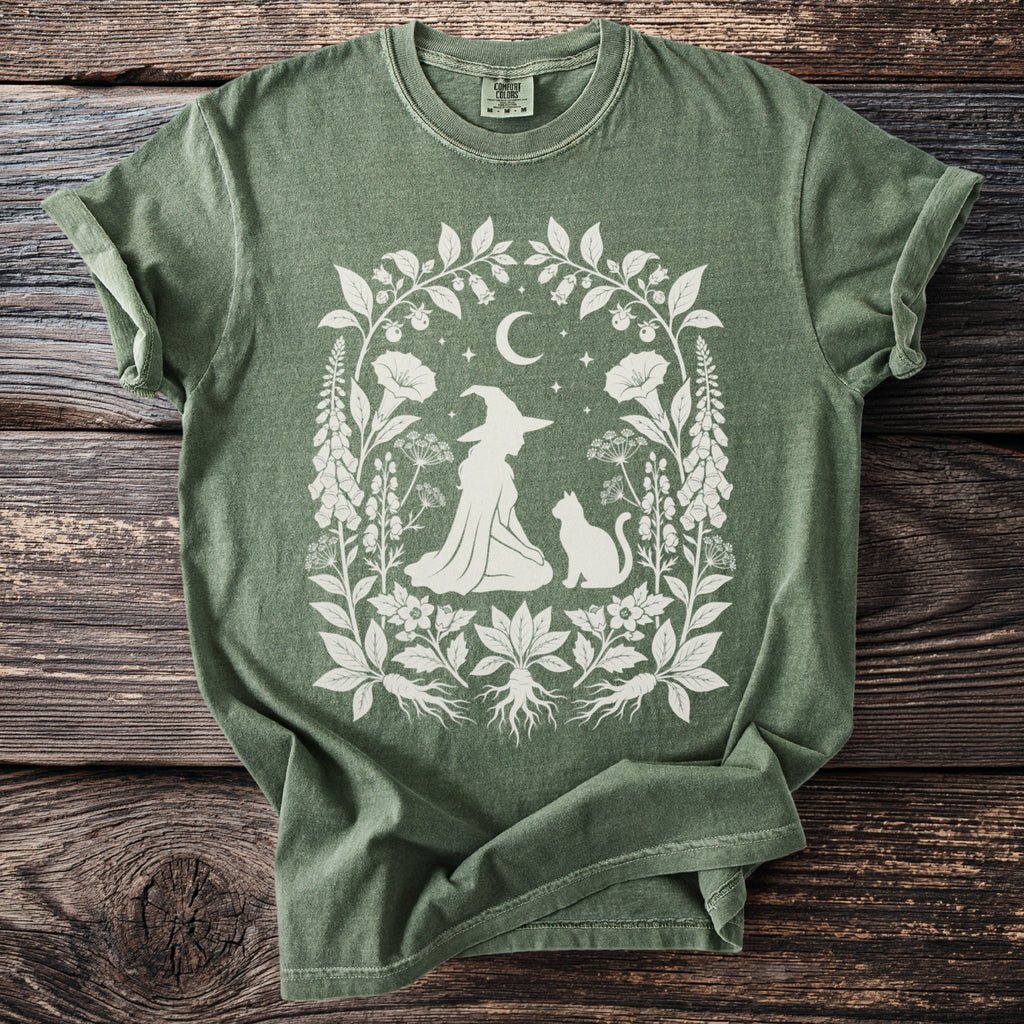 Green t-shirt with white witch, cat, moon, stars, and botanical floral design.