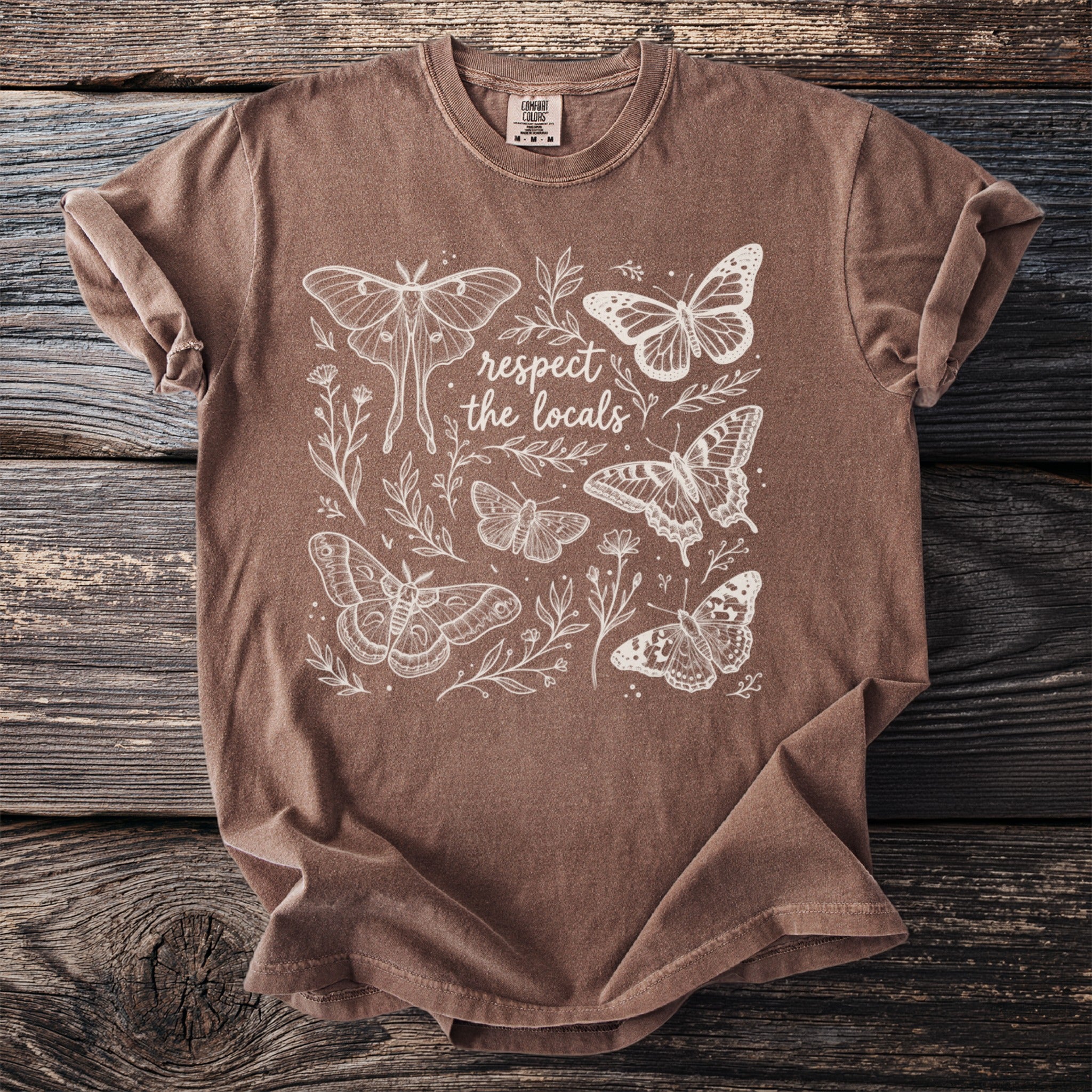 Brown t-shirt with white line art illustration of moths, butterflies, and floral elements, with "respect the locals" text.