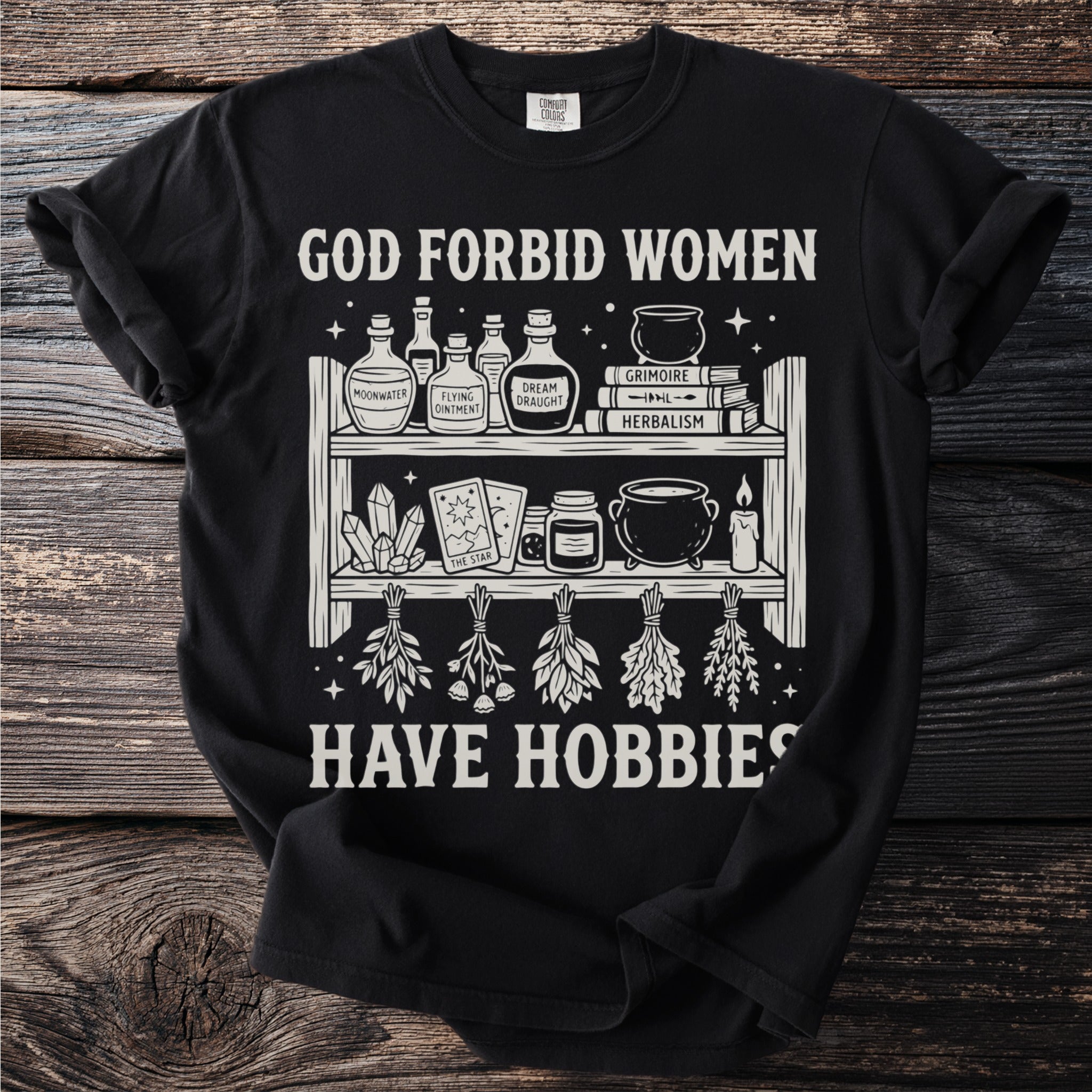 Black t-shirt with text "God forbid women have hobbies" and witchy illustrations.