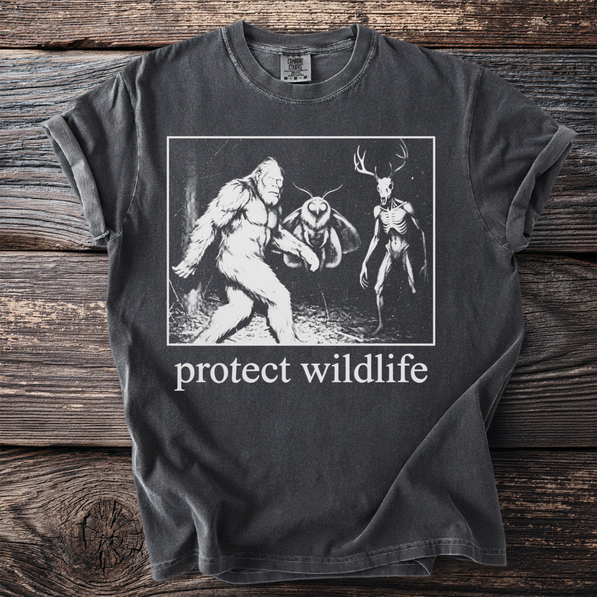 T-shirt with Bigfoot, mothman, and deer skull graphic and "protect wildlife" text.