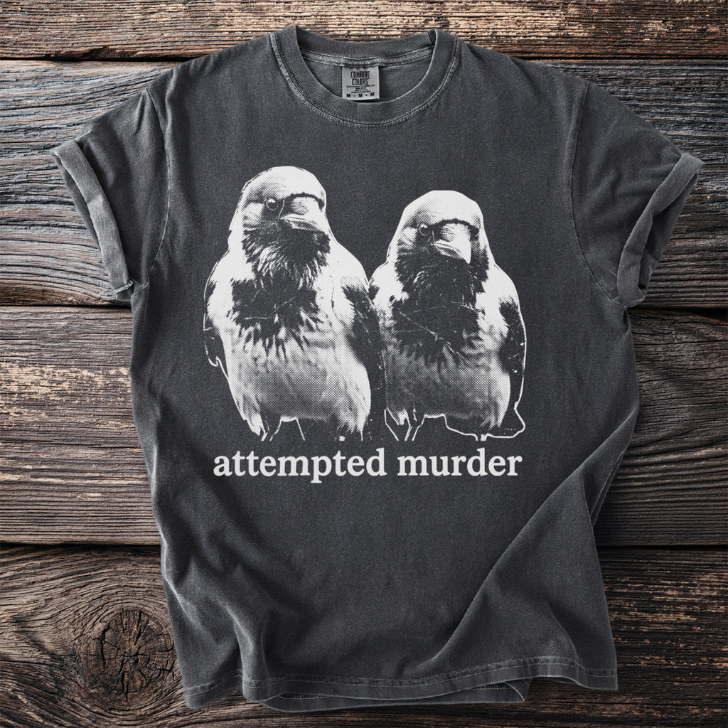 Dark gray t-shirt with a black and white graphic of two birds and "attempted murder" text.