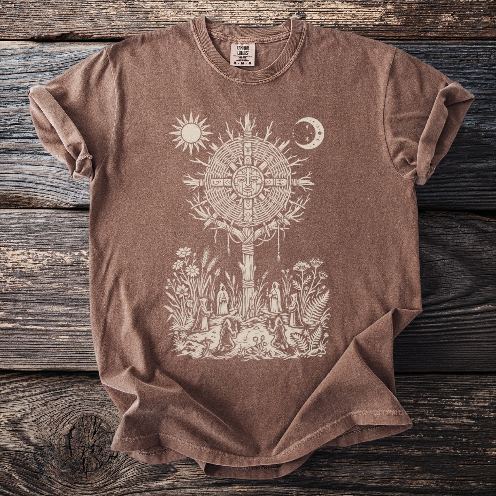 Brown t-shirt with a cream graphic of a sun and moon over a ritual scene.