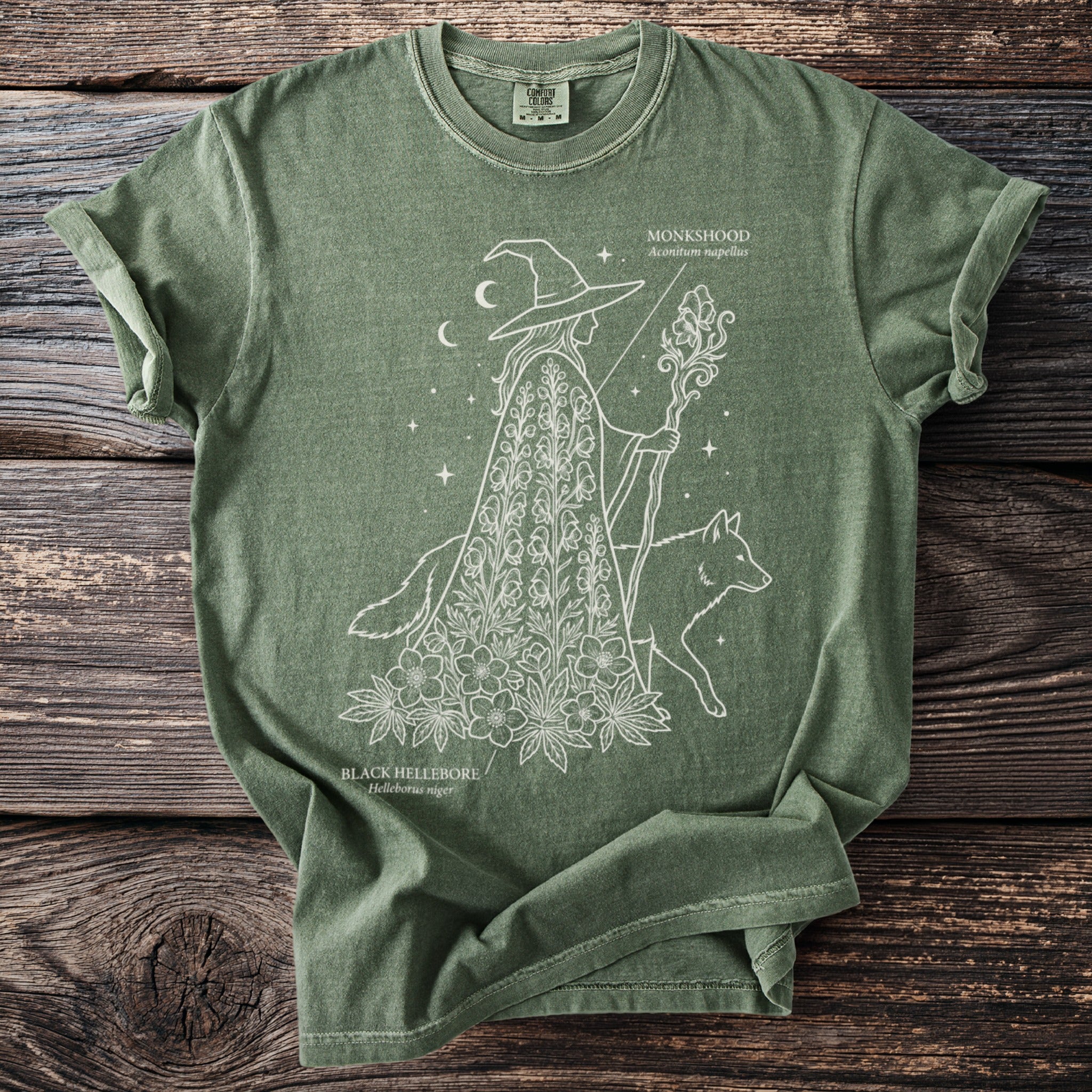 Green t-shirt with white line art of a witch, a fox, and botanical elements.