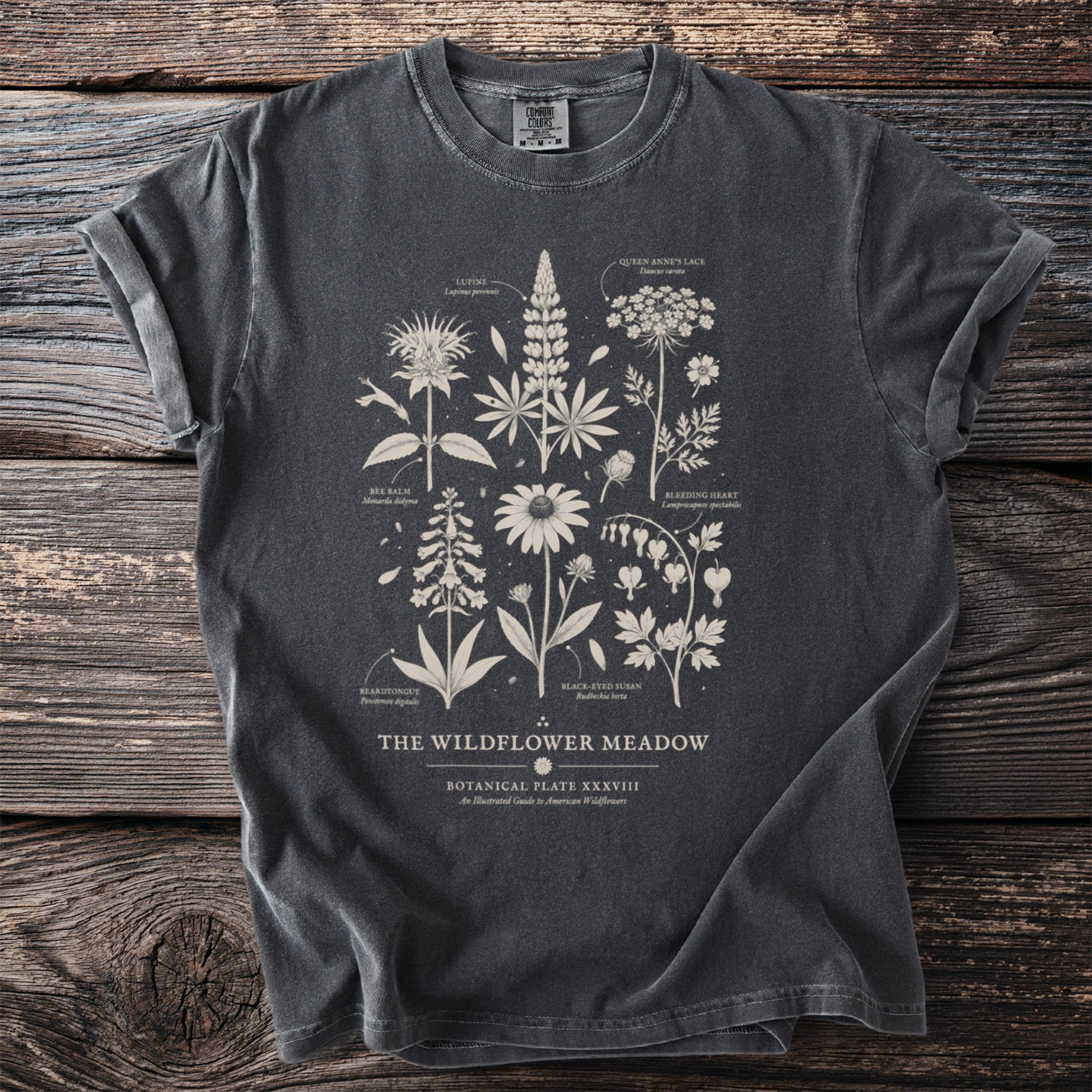 Dark t-shirt with "The Wildflower Meadow" botanical illustration featuring labeled wildflowers and scientific names.