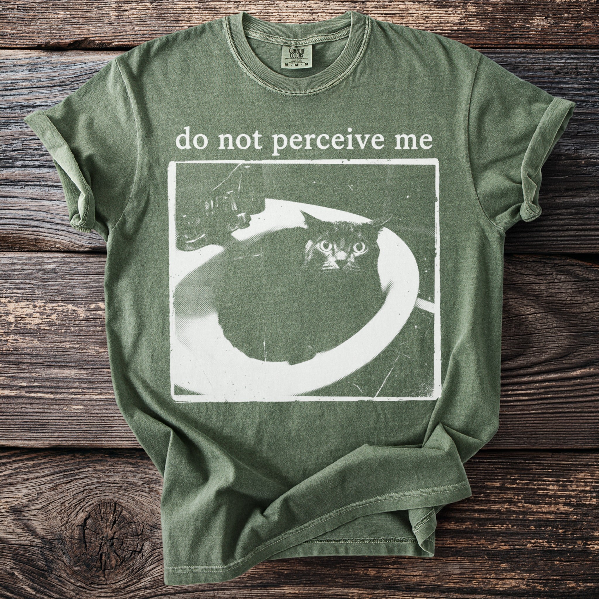 Green t-shirt with distressed print of a cat in a sink and "do not perceive me".