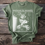 Green t-shirt with white graphic of a wolf holding a baby, "nocturnal by necessity" text.