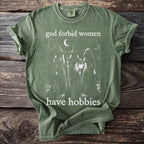 Olive green t-shirt with witches and bats graphic and text: "god forbid women have hobbies".