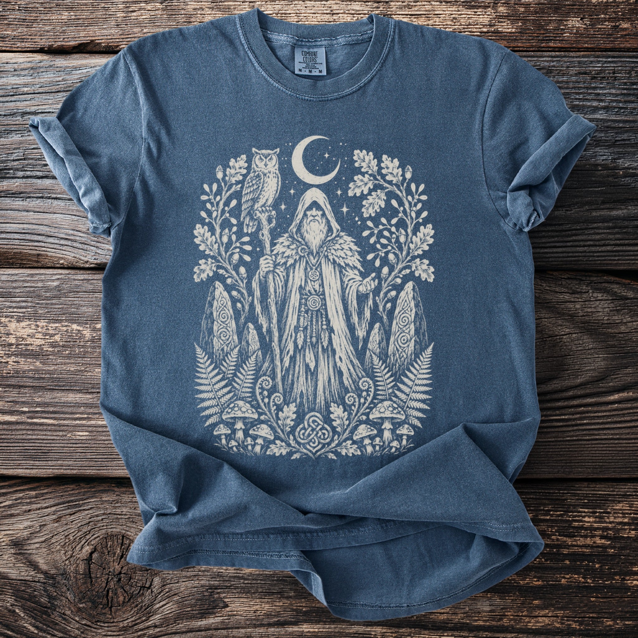 Blue t-shirt with cream print of a wizard with an owl, moon, and forest elements.