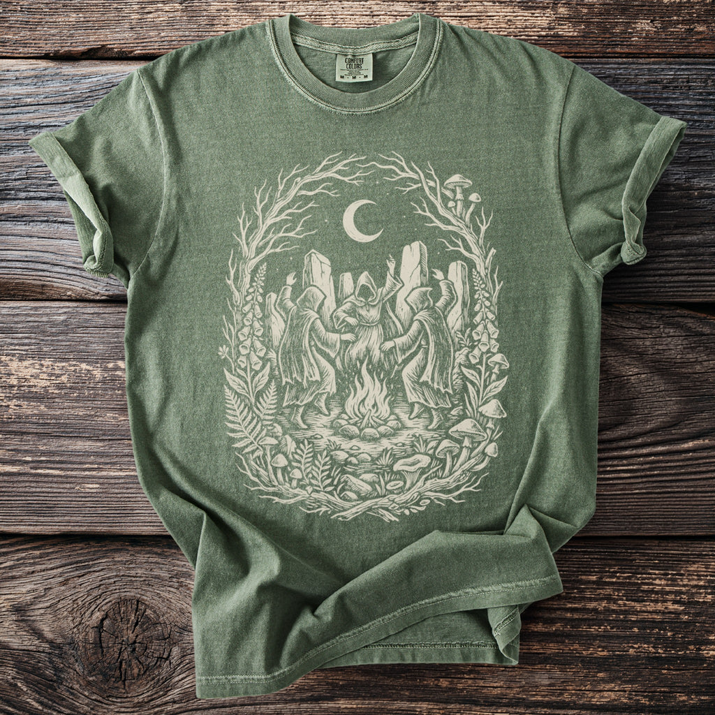 Green t-shirt with a cream-colored witchy coven dancing around a bonfire under a moon.