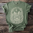 Green t-shirt with a cream-colored witchy coven dancing around a bonfire under a moon.