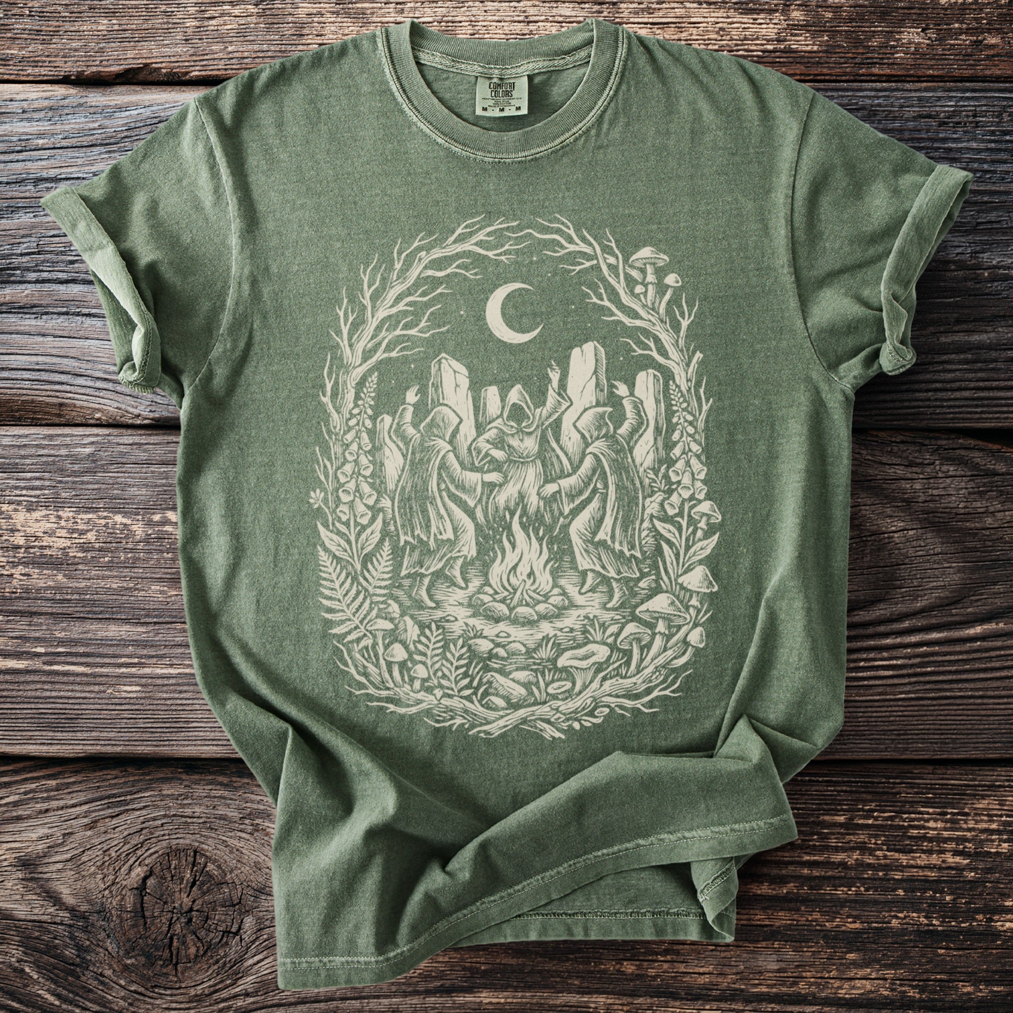 Green t-shirt with a cream-colored witchy coven dancing around a bonfire under a moon.