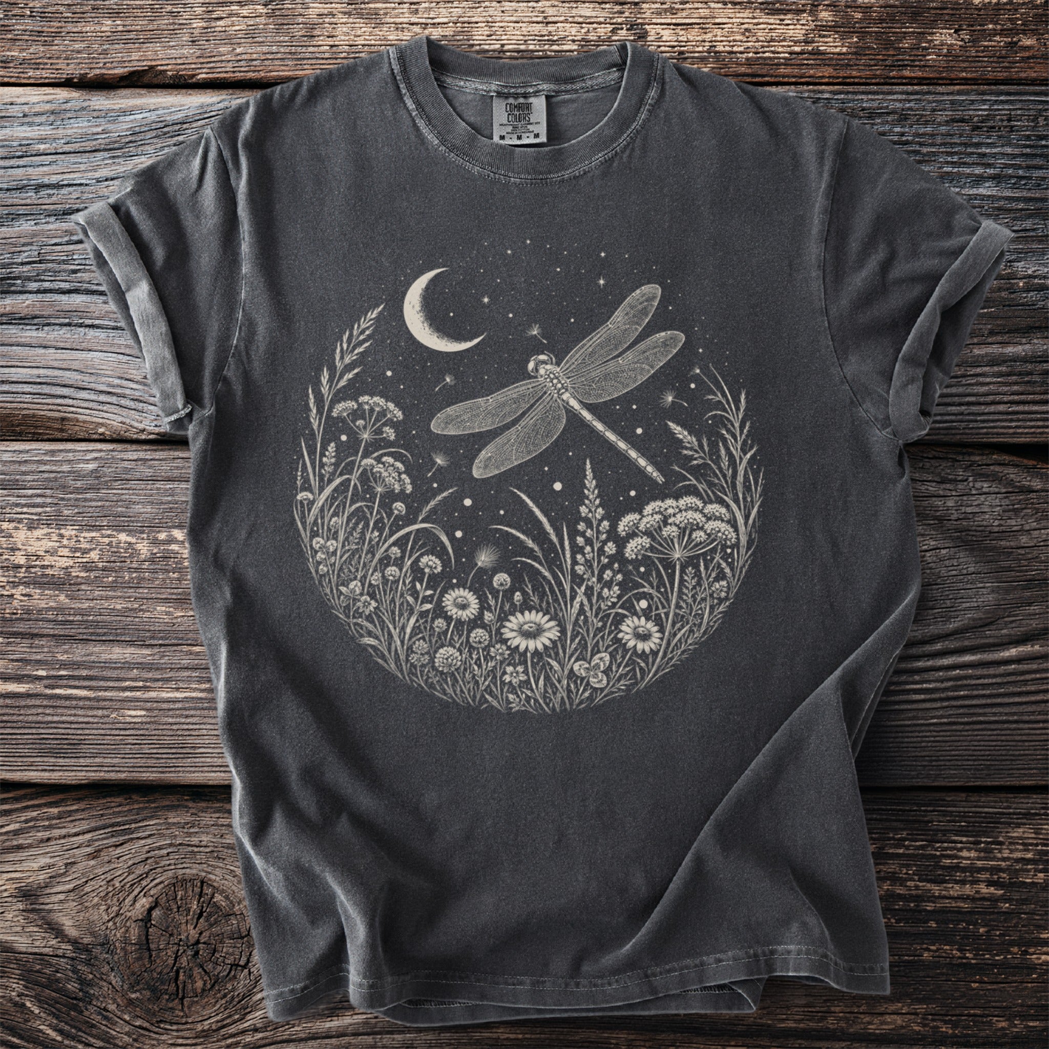 Dark t-shirt with a circular print of a dragonfly, moon, and wildflowers under a starry sky.