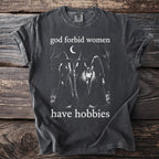 Dark grey t-shirt with white text "god forbid women have hobbies" and three witches graphic.
