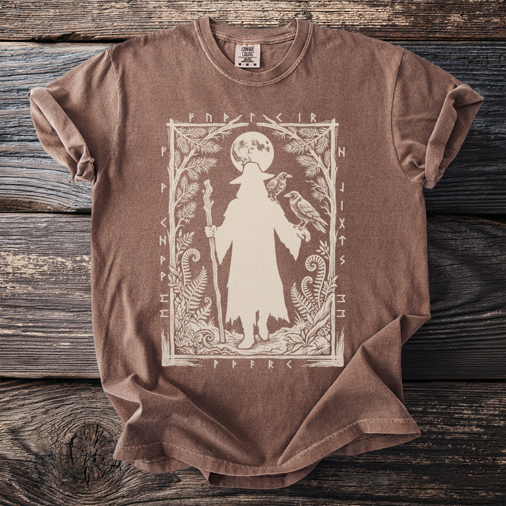 Brown t-shirt with a silhouette of a figure holding a staff and two ravens, surrounded by foliage and runes.