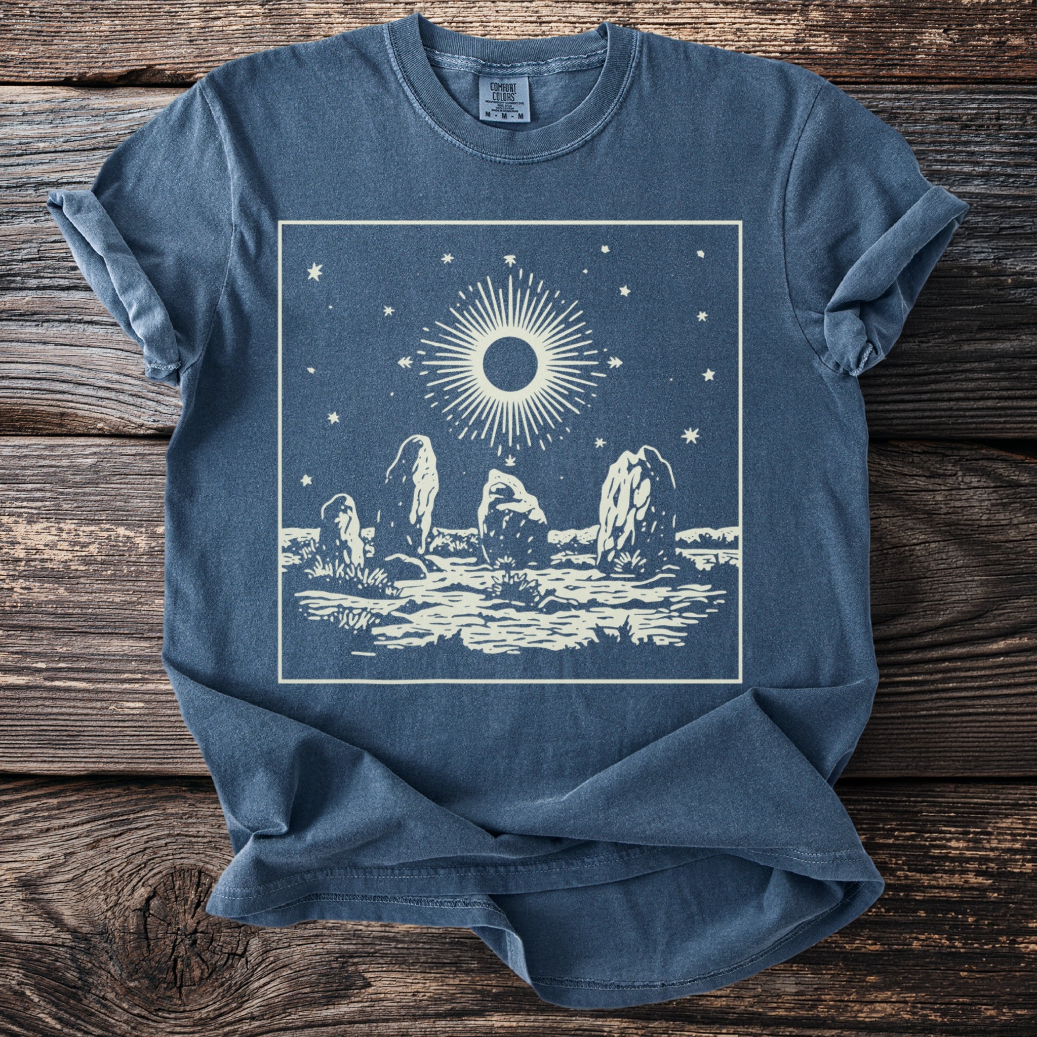 Blue t-shirt with cream circular sun and standing stones graphic.