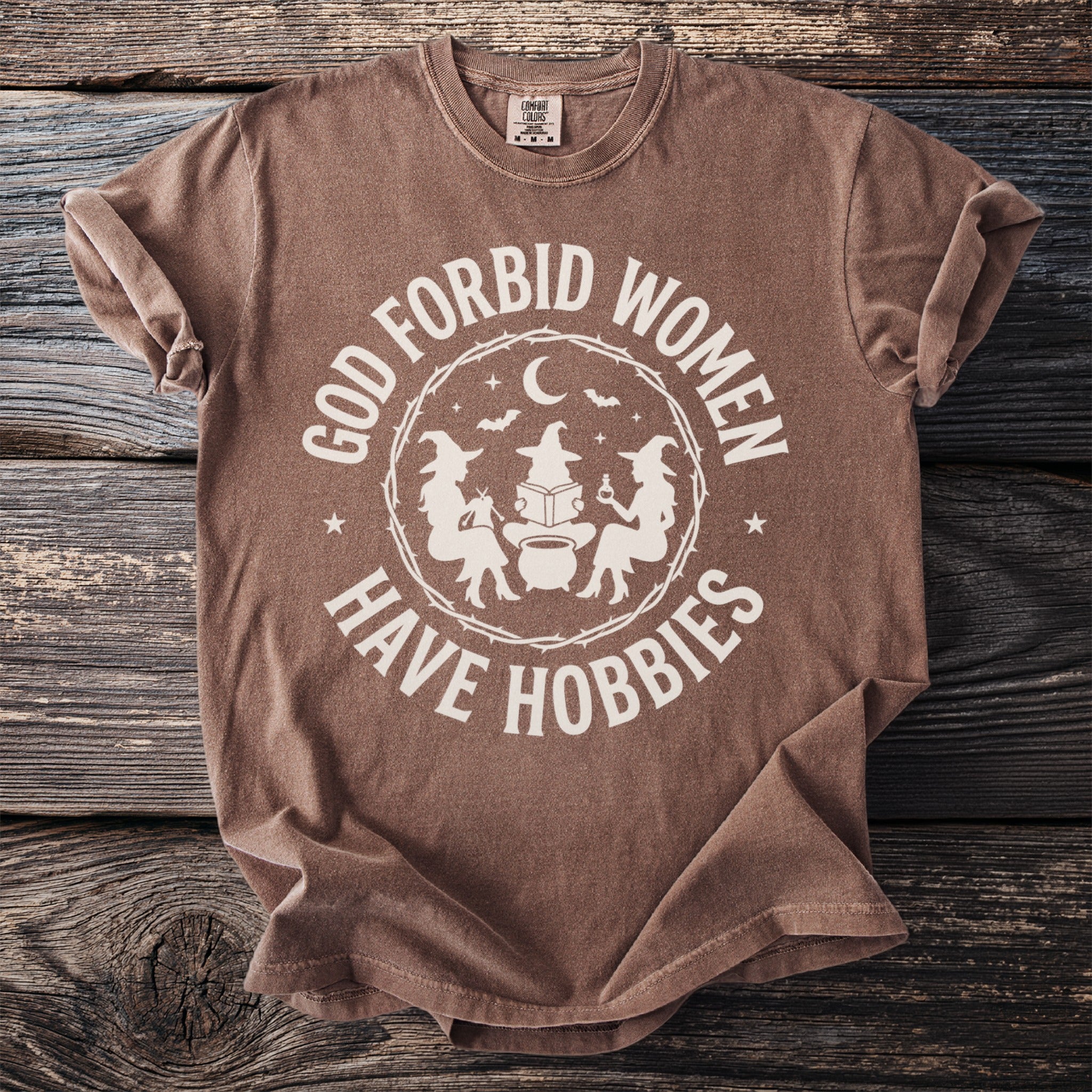 Brown t-shirt with graphic reading "God forbid women have hobbies" and witches.