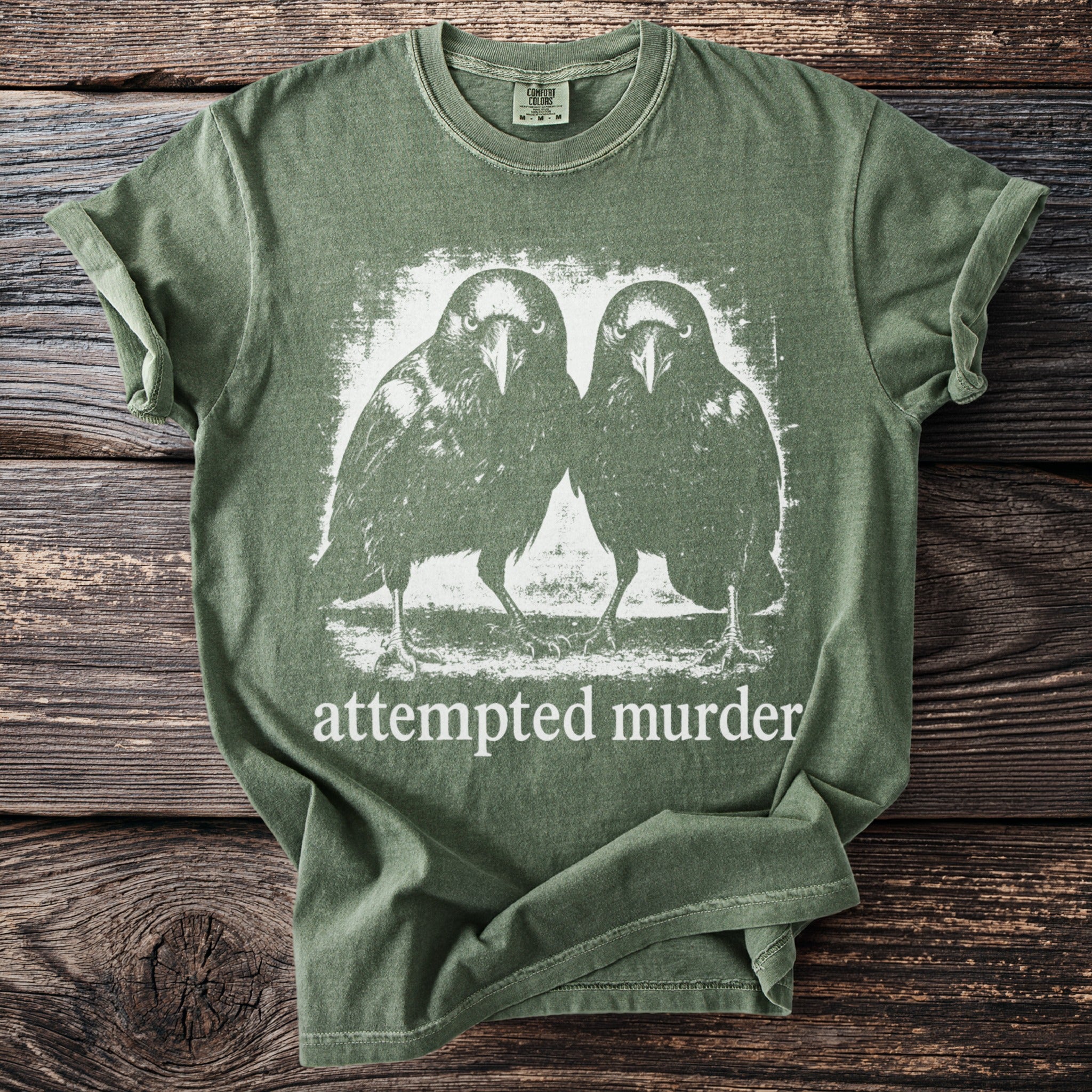 Green t-shirt with graphic of two crows and text "attempted murder".