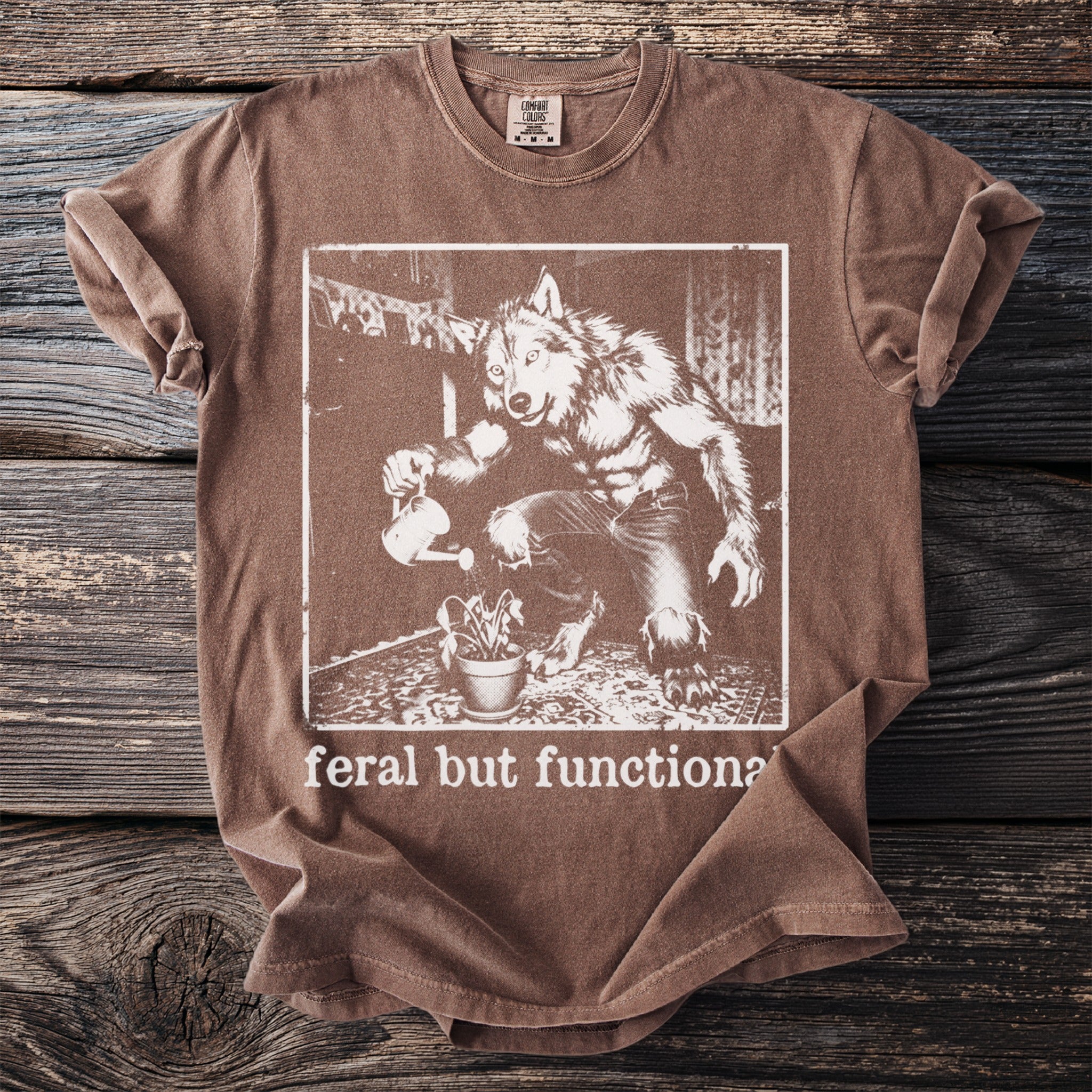 Brown t-shirt with werewolf watering a plant and text "feral but functional".