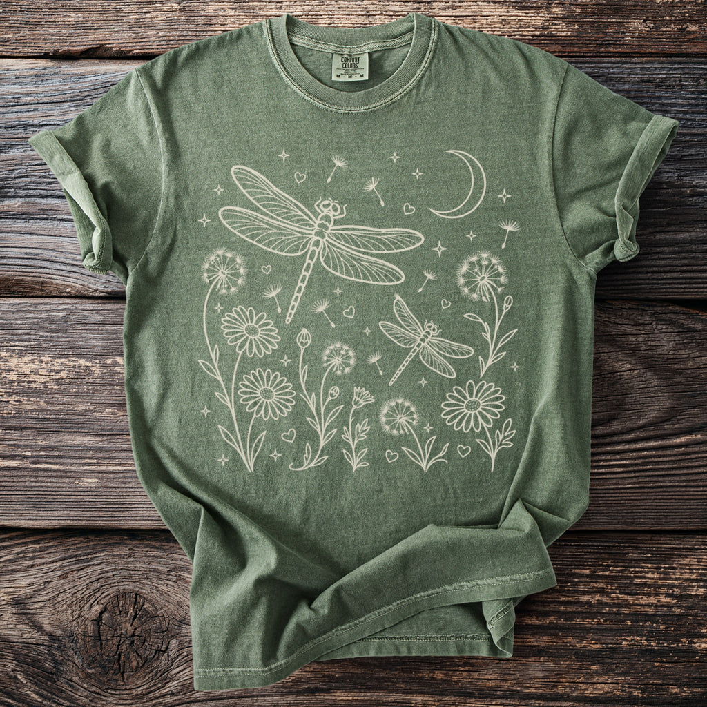 Green t-shirt with white line art of dragonflies, flowers, dandelions, and a crescent moon.
