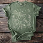 Green t-shirt with white line art of dragonflies, flowers, dandelions, and a crescent moon.