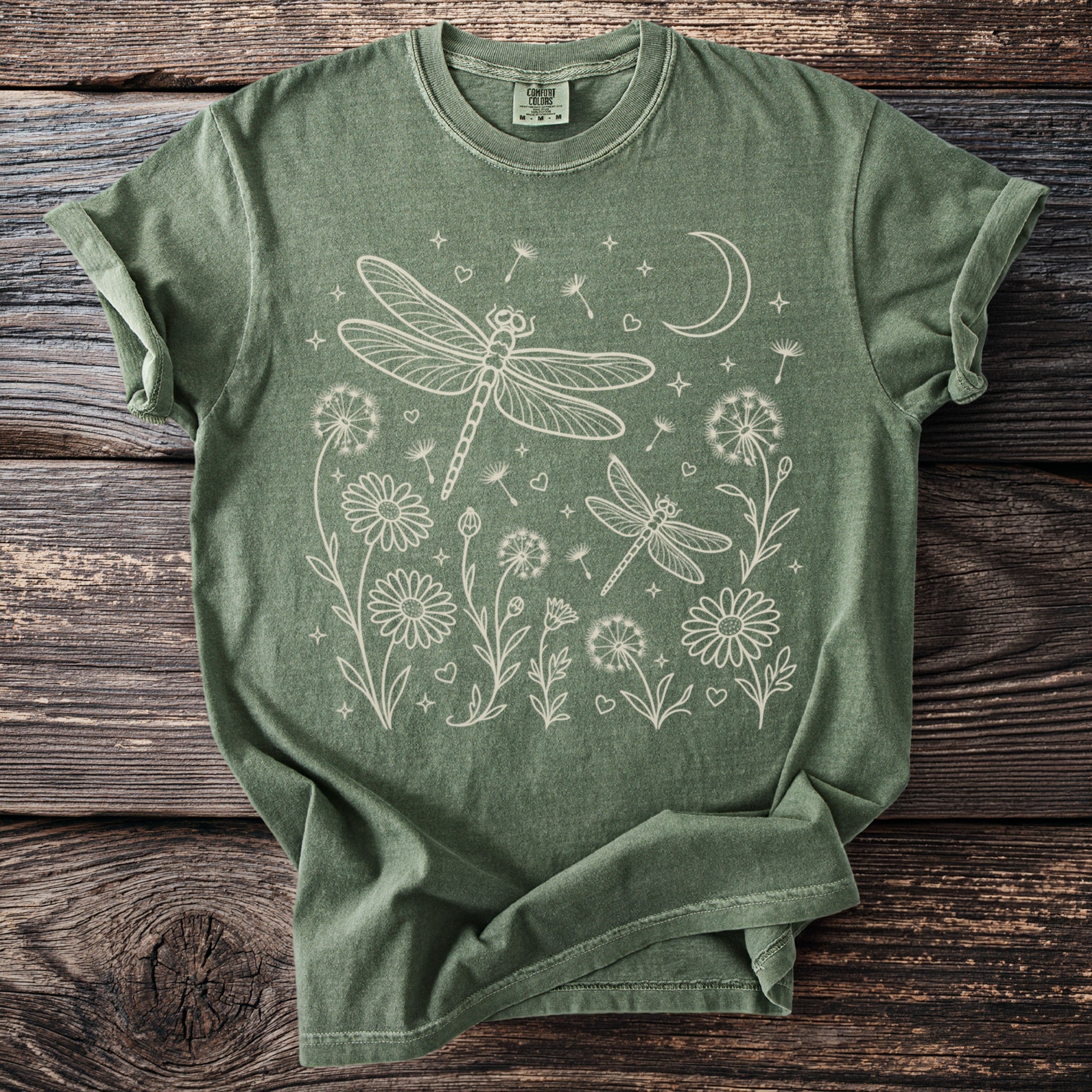 Green t-shirt with white line art of dragonflies, flowers, dandelions, and a crescent moon.