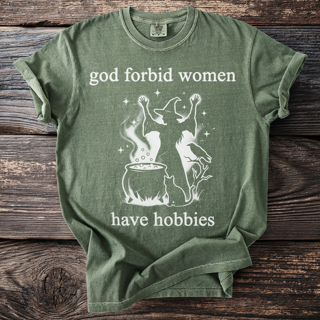 Green t-shirt with white text saying "god forbid women have hobbies" and witch graphic.
