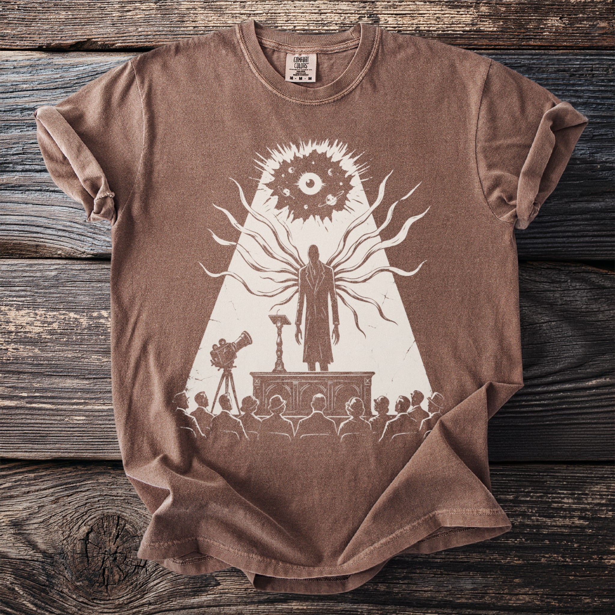 Brown t-shirt featuring a print of a tall, slender figure with tentacles and an eye in the sky.