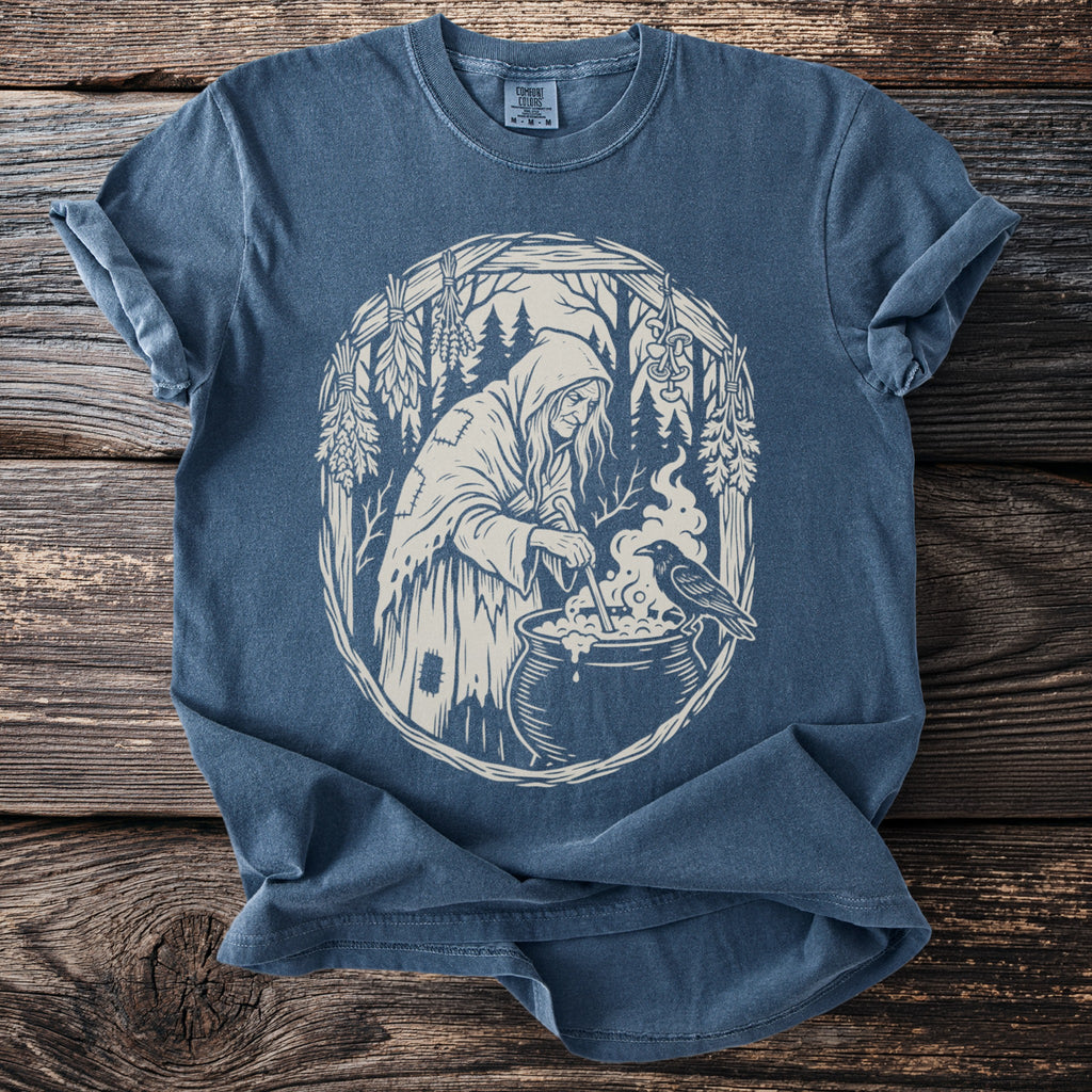 T-shirt with cream design of a witch stirring cauldron with a crow beside it.