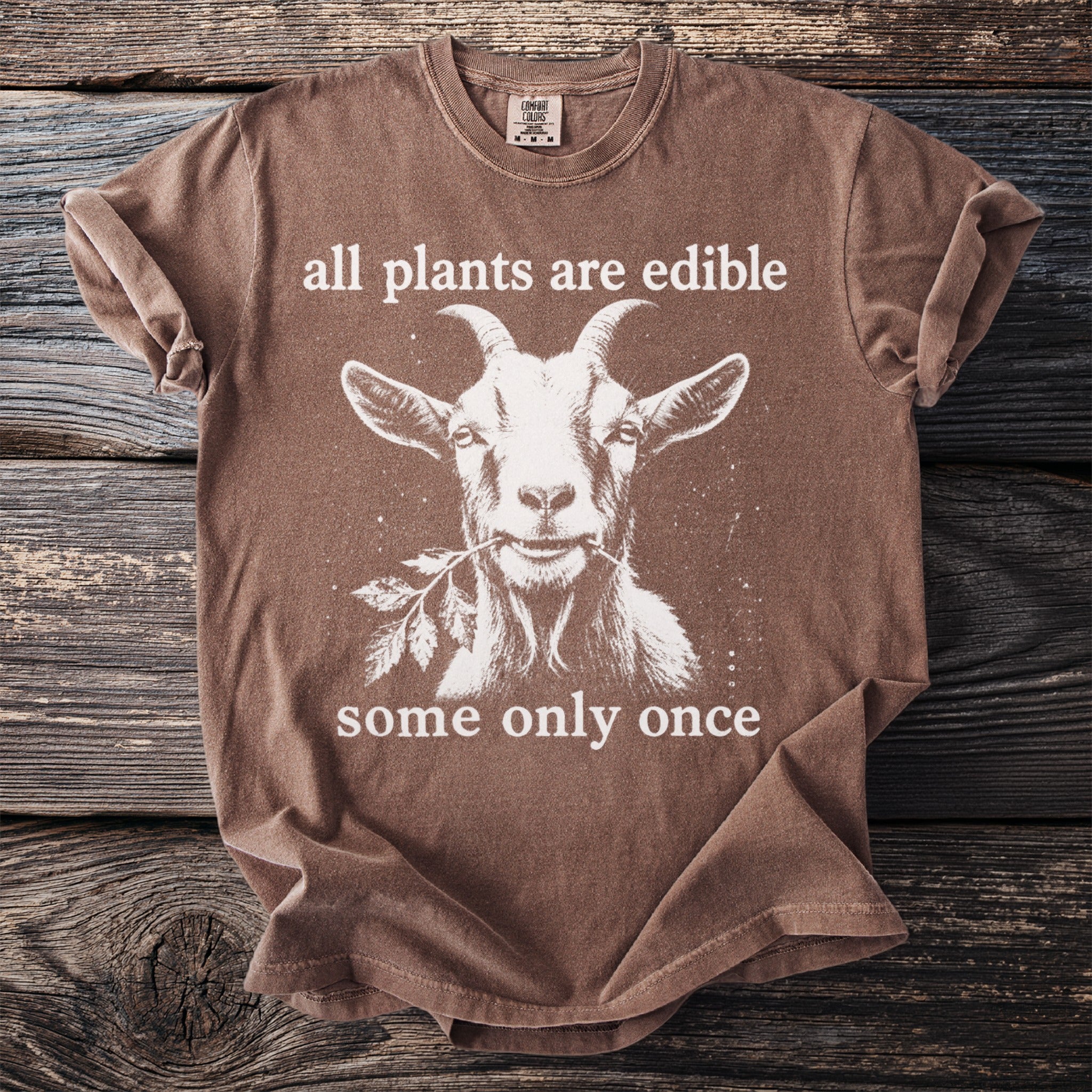 Brown t-shirt with a goat graphic and text: "all plants are edible, some only once."