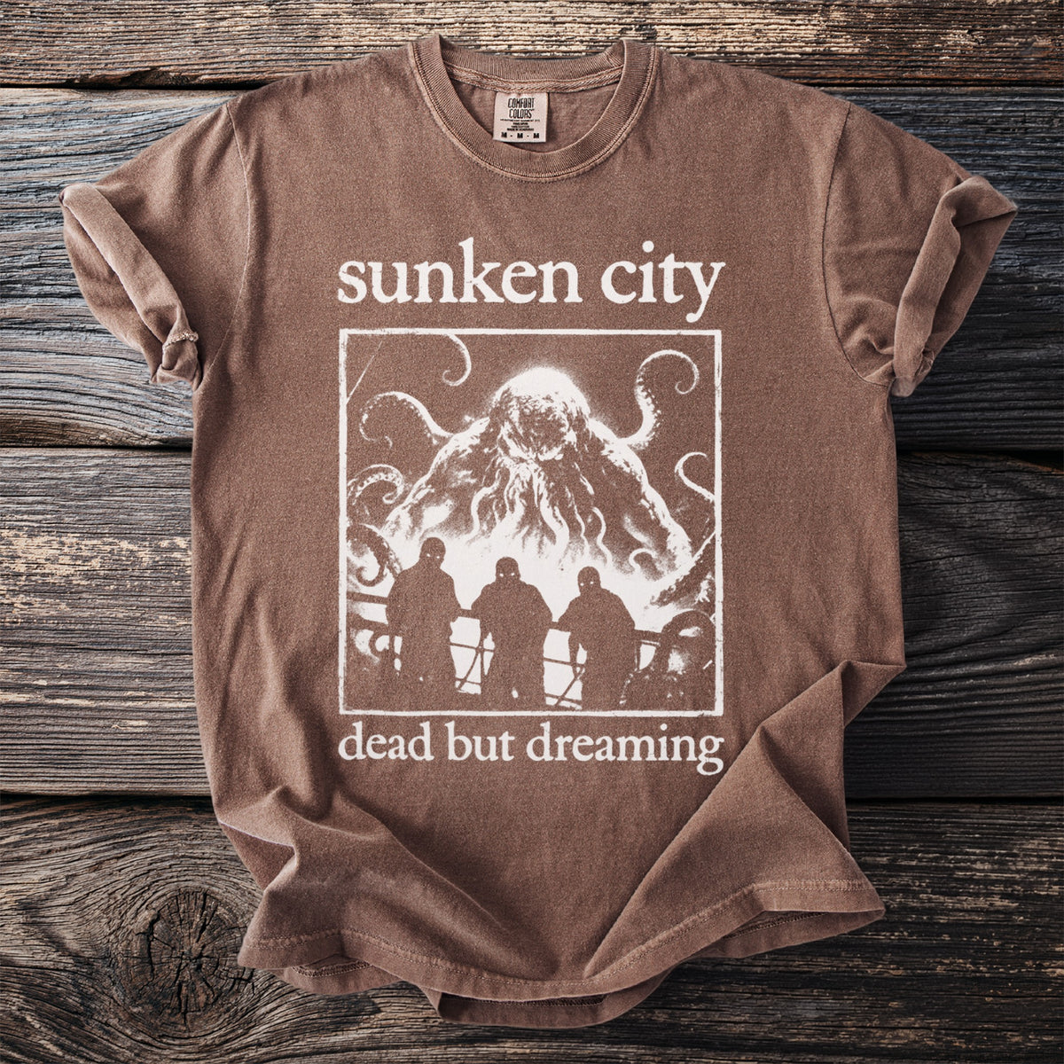 Brown t-shirt with "sunken city dead but dreaming" and kraken artwork.