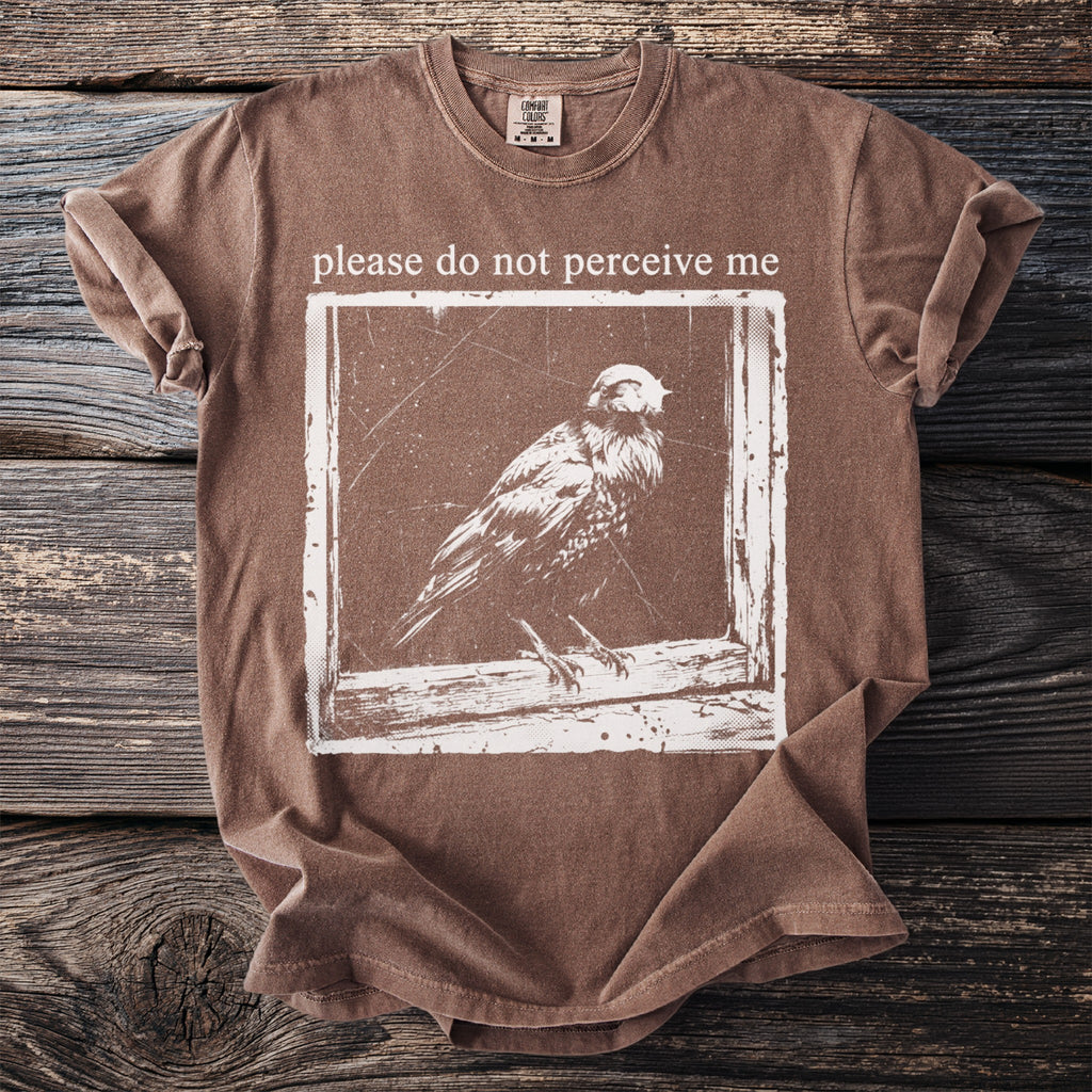Brown t-shirt with white graphic of a bird and text "please do not perceive me."