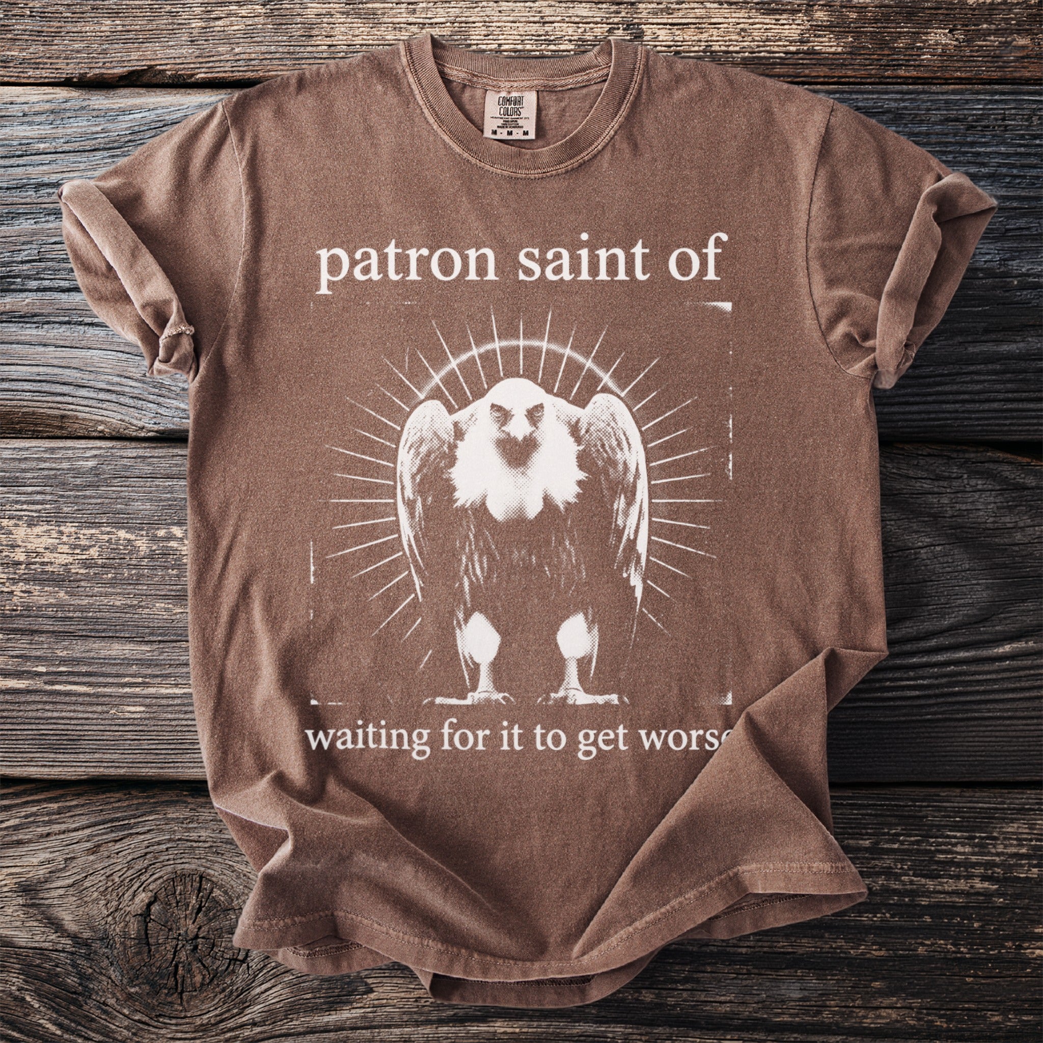Brown t-shirt with white text "patron saint of" and a vulture graphic.
