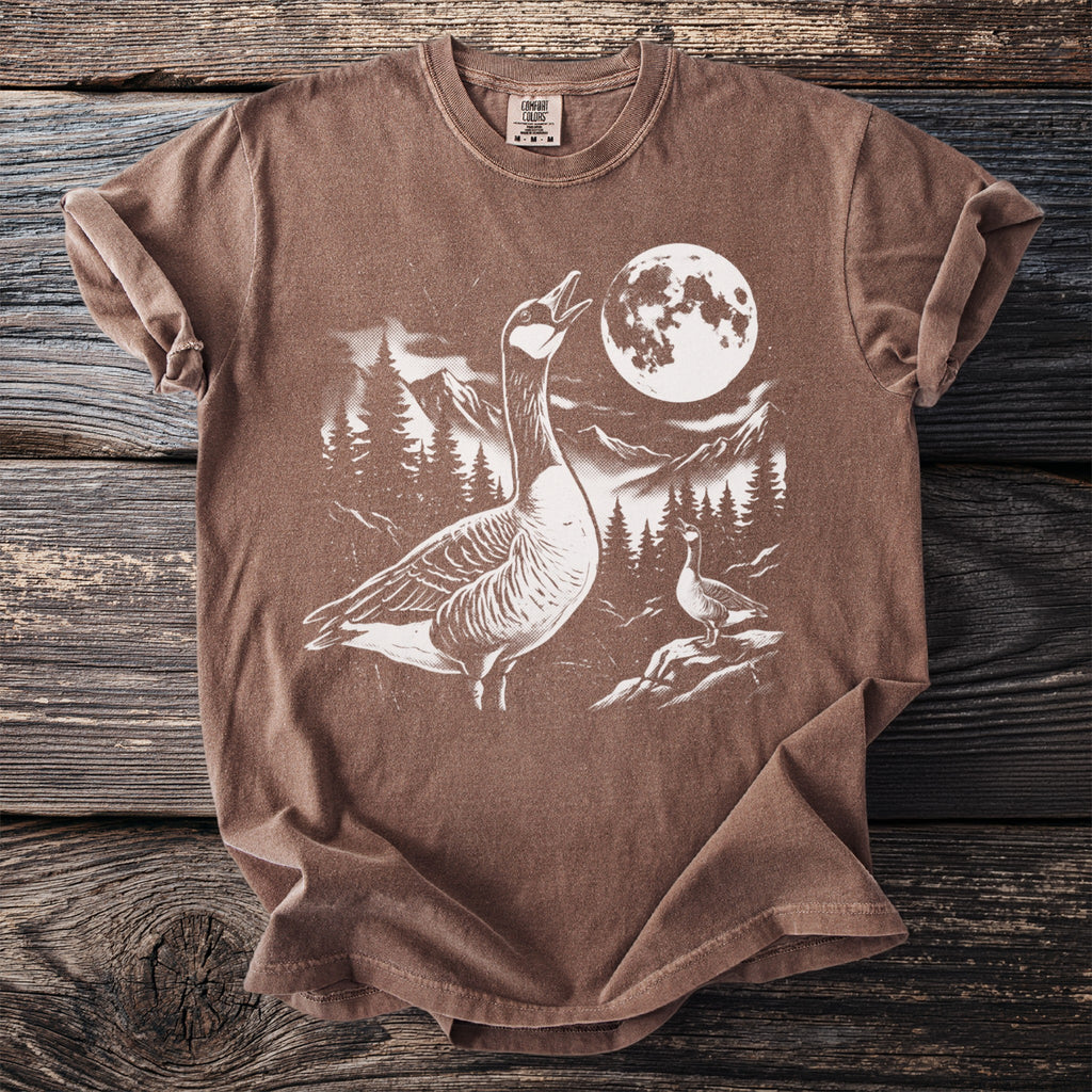 Brown t-shirt with white graphic of two geese, moon, mountains, and pine trees.