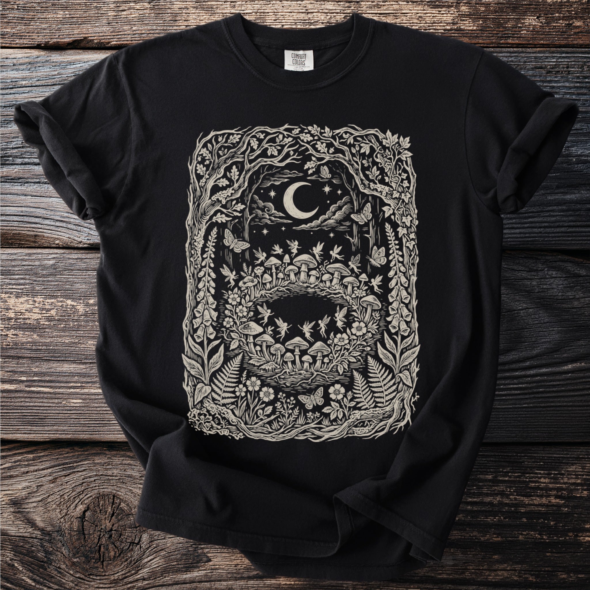 Black t-shirt with a detailed linocut print of a whimsical forest scene at night with a moon.