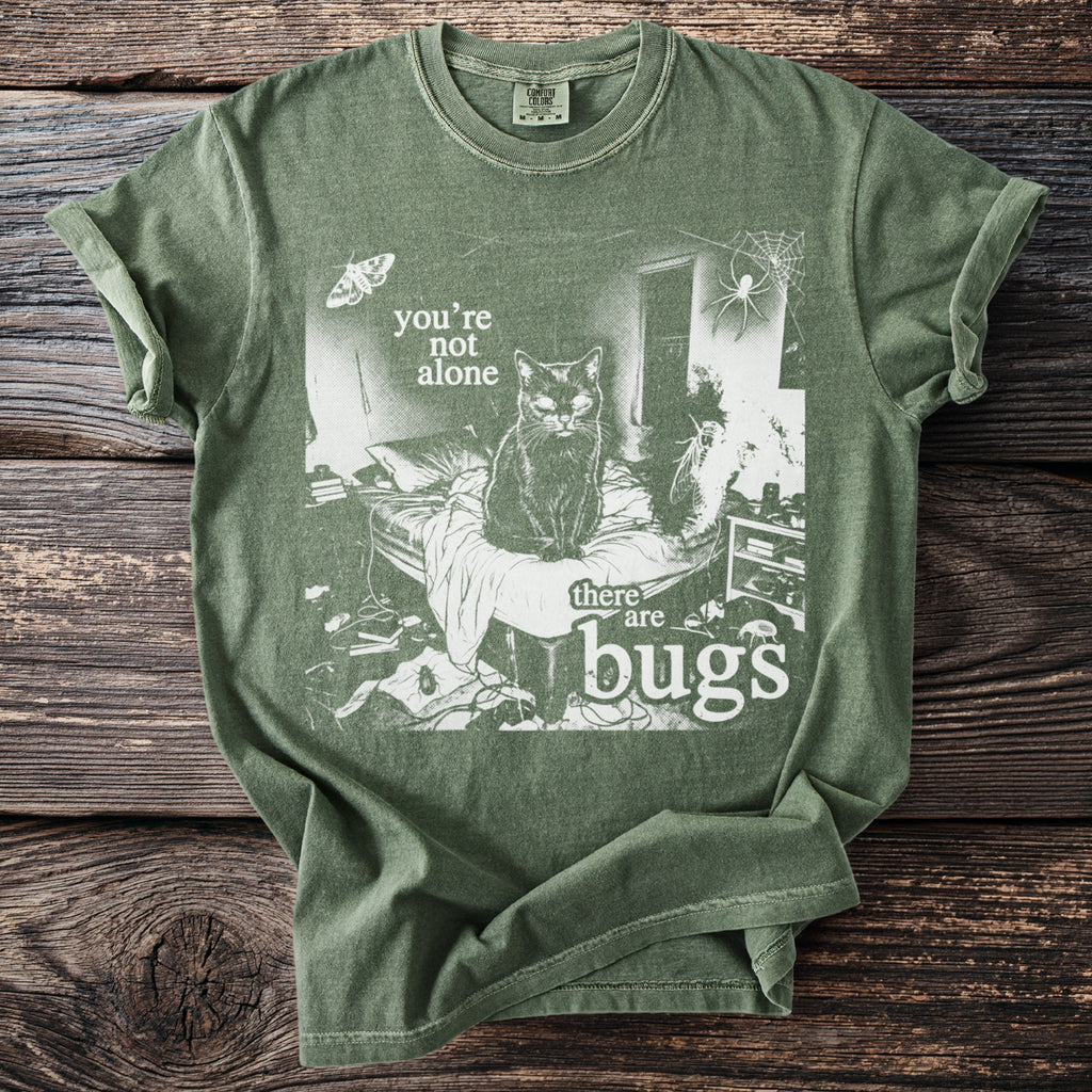 Green t-shirt with a black cat, spider, moth, and text reading "you're not alone there are bugs".