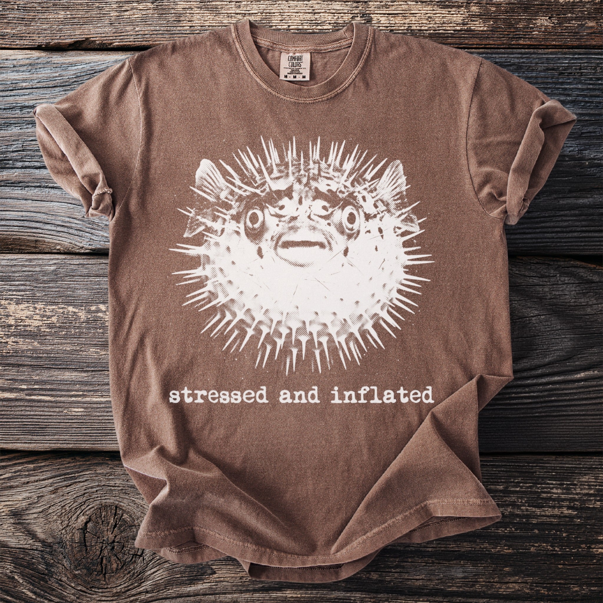 Brown t-shirt with distressed print of a spiky pufferfish and text "stressed and inflated".