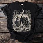 Three cloaked figures surround a bonfire beneath a crescent moon, with trees and foliage.