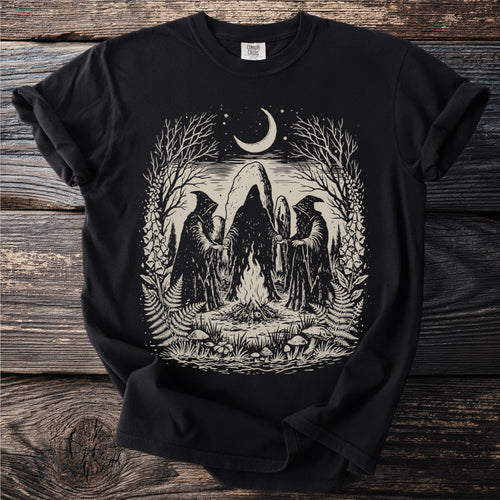 Three cloaked figures surround a bonfire beneath a crescent moon, with trees and foliage.