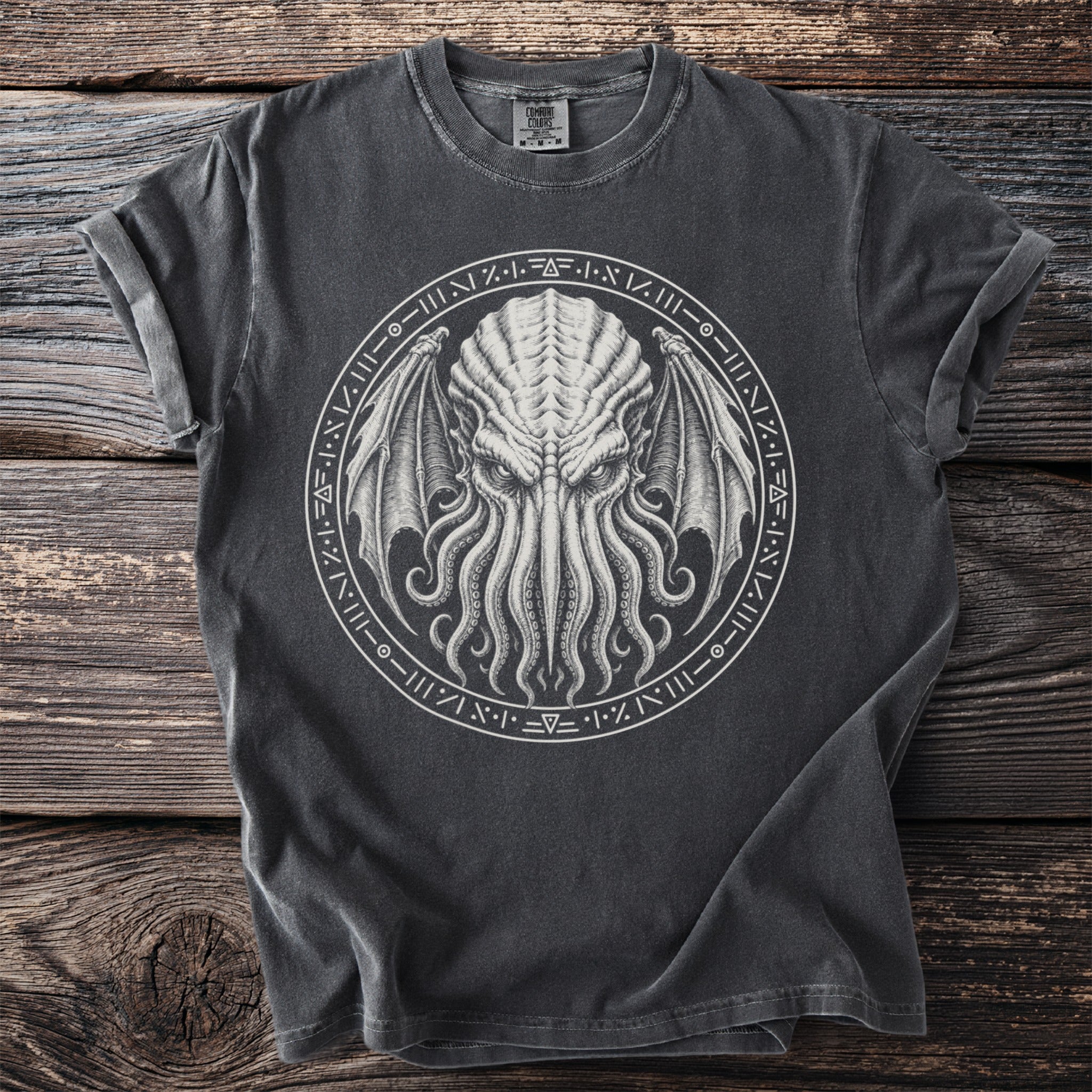 Dark grey t-shirt with a tentacled creature and occult symbols on a rustic wooden background.