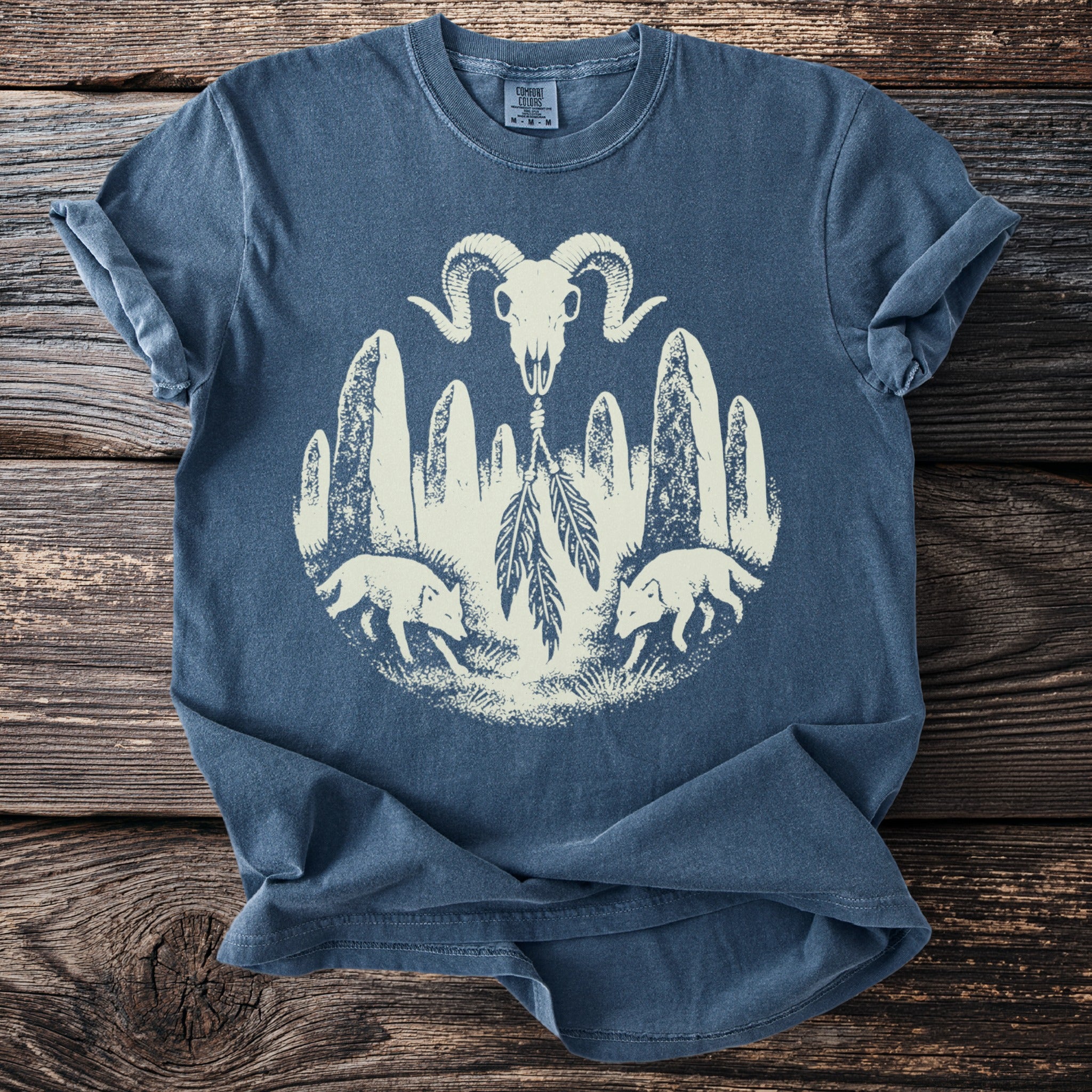 Blue t-shirt with graphic of ram skull, standing stones, foxes, and feathers.