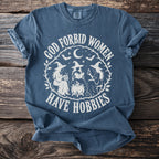 Blue t-shirt with white graphic "God Forbid Women Have Hobbies" and witches.