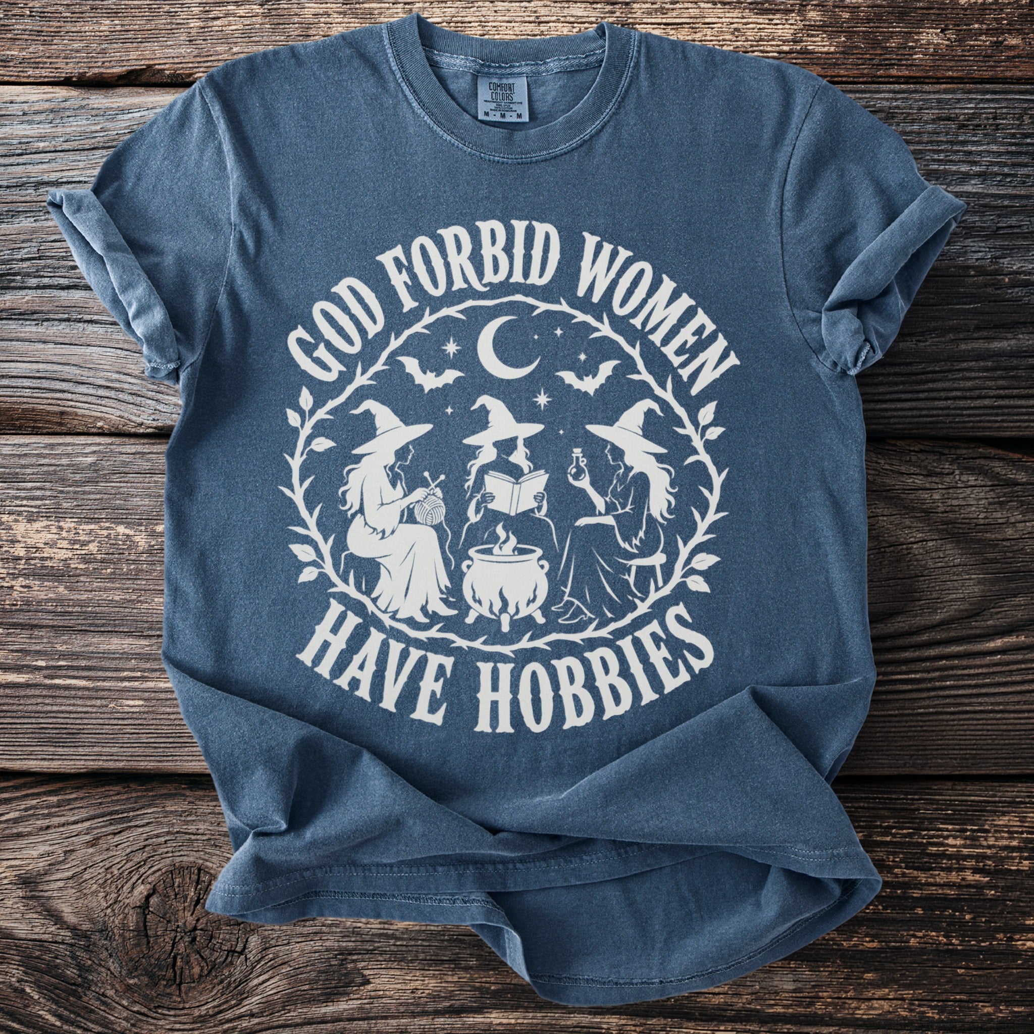 Blue t-shirt with white graphic "God Forbid Women Have Hobbies" and witches.